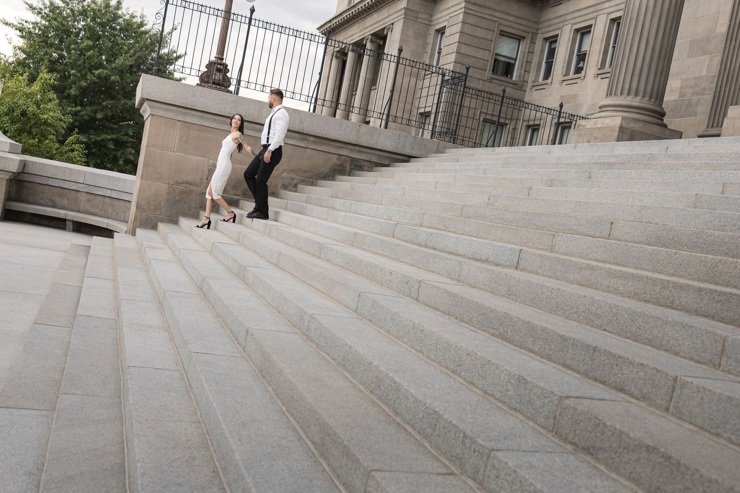 Architectural view of sweeping stone staircase with trees and railing.