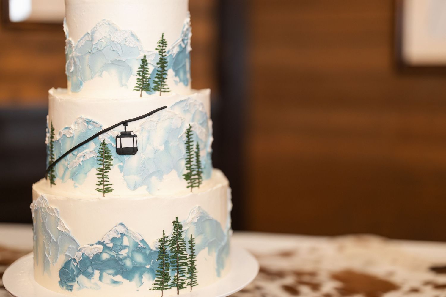 A winter-themed wedding cake decorated with blue watercolor and pine trees.