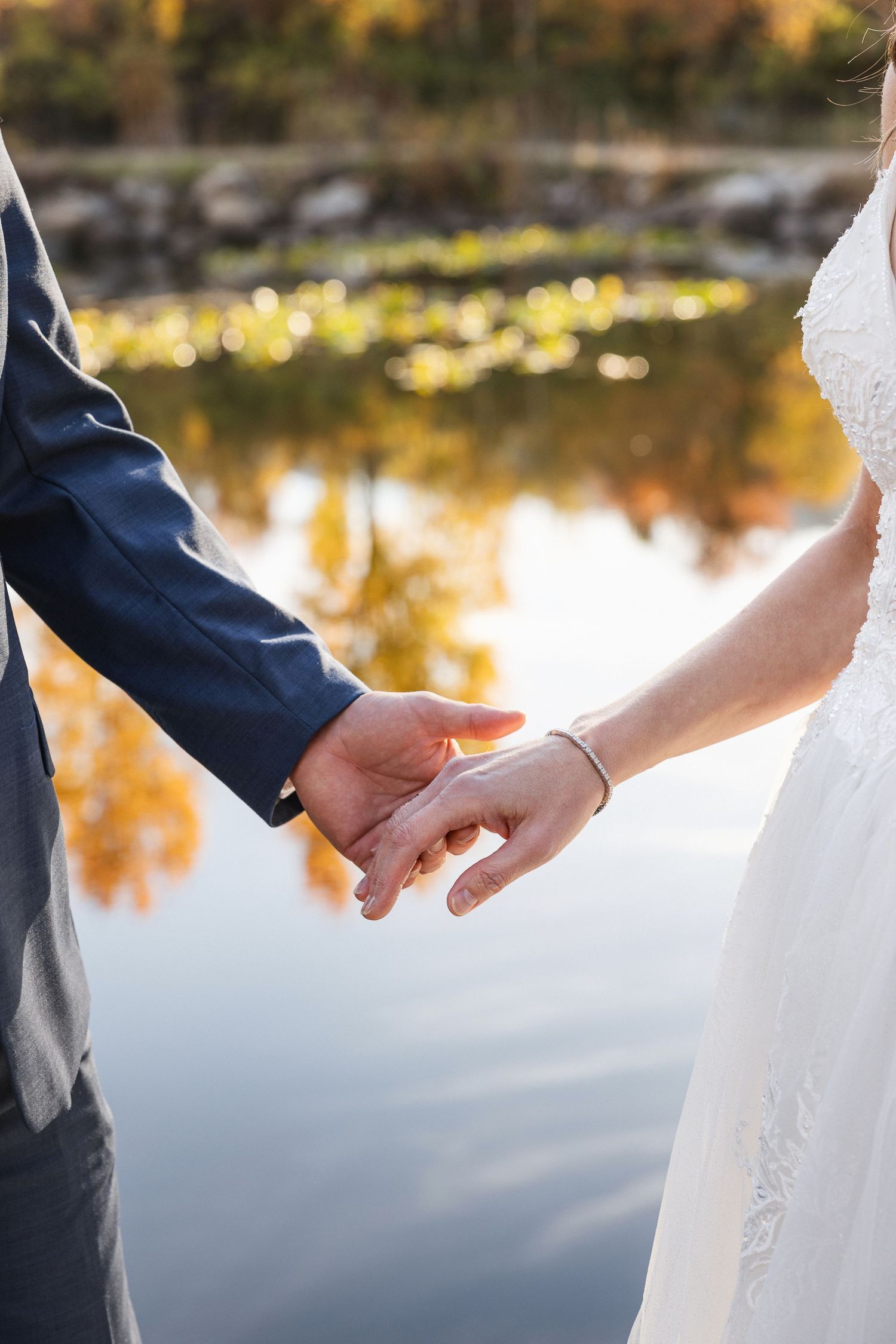 Intimate shot of newlyweds holding hands by a reflective pond at sunset.