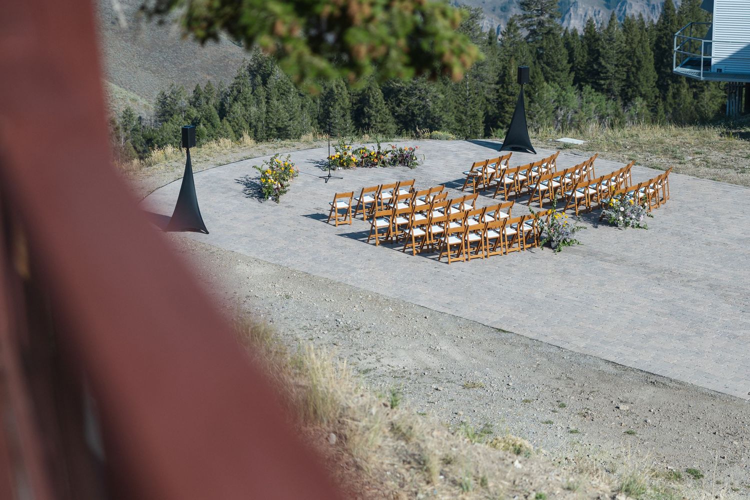 A rustic outdoor wedding ceremony setup with wooden chairs arranged in rows on a gravel surface surrounded by trees.