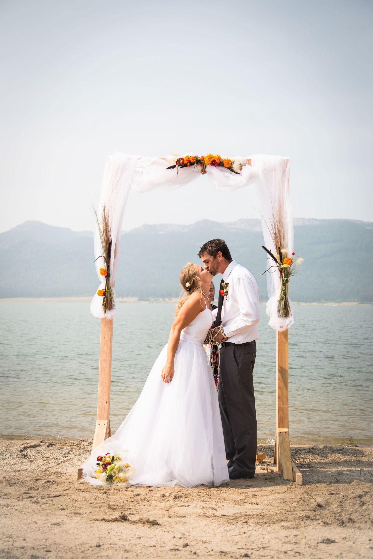 Wedding couple sharing a tender moment under a simple beach arch with mountain views.