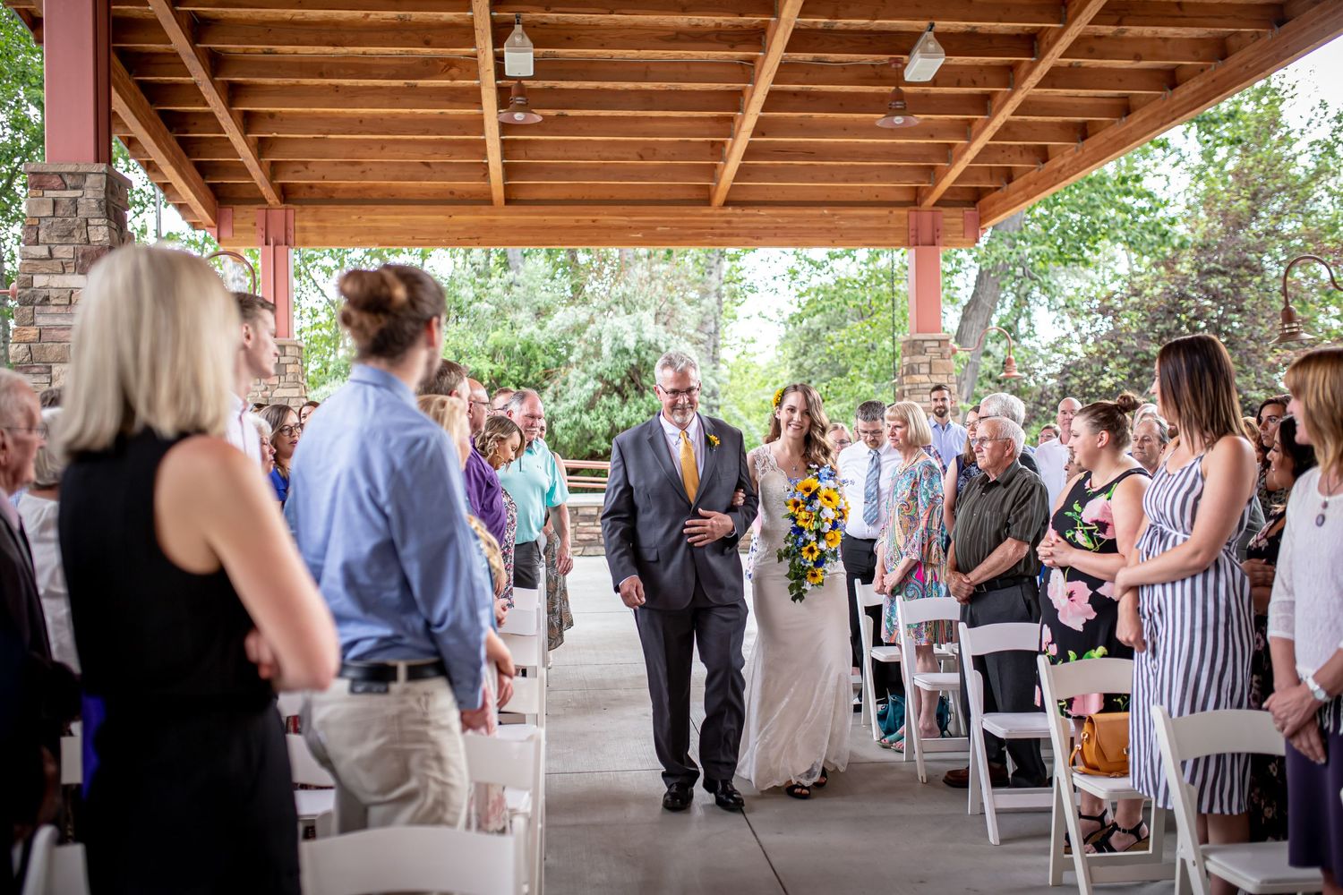 Guests gathered under a wooden pergola during an outdoor wedding ceremony.