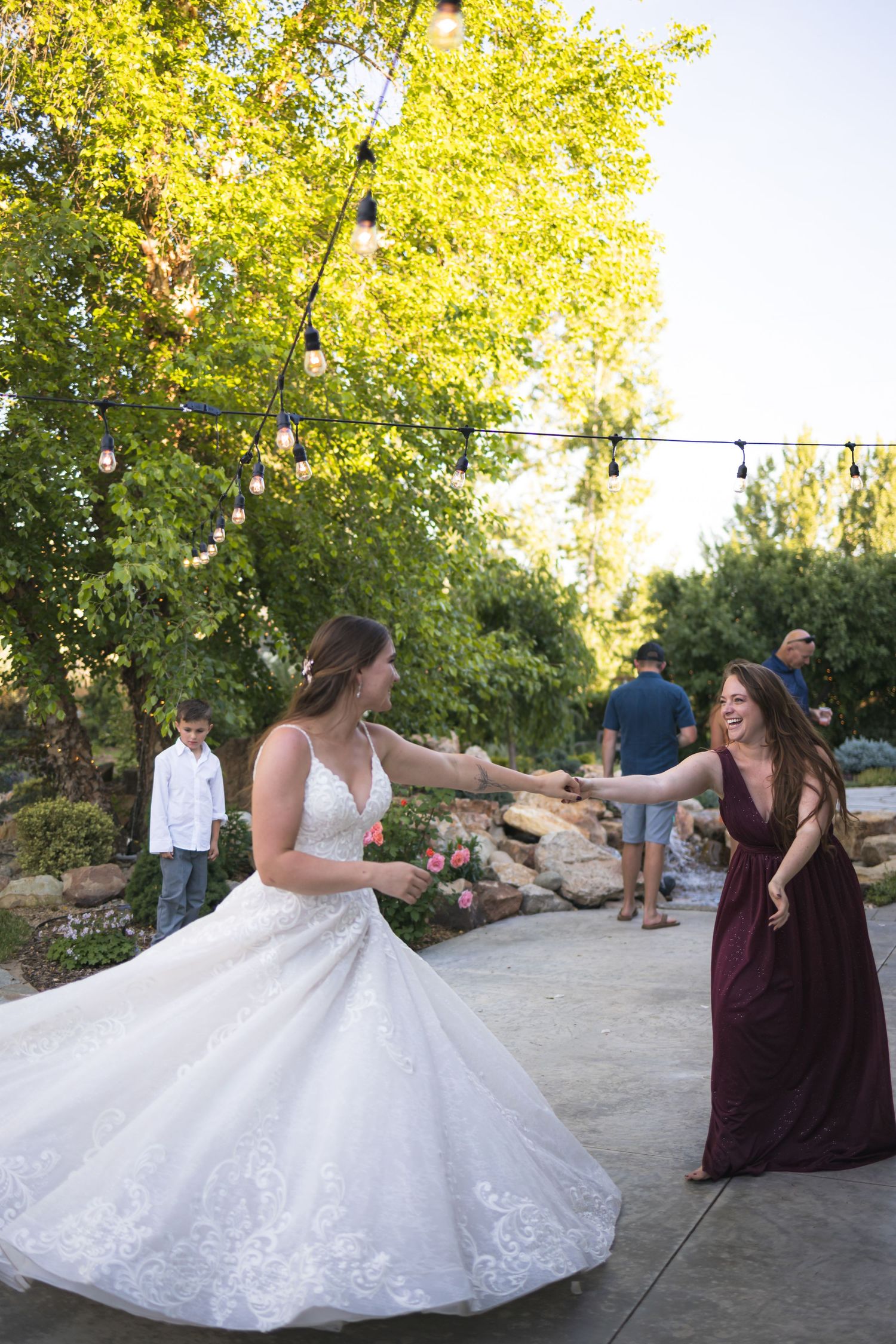 Wedding guests dancing outdoors under string lights and trees during a celebration.