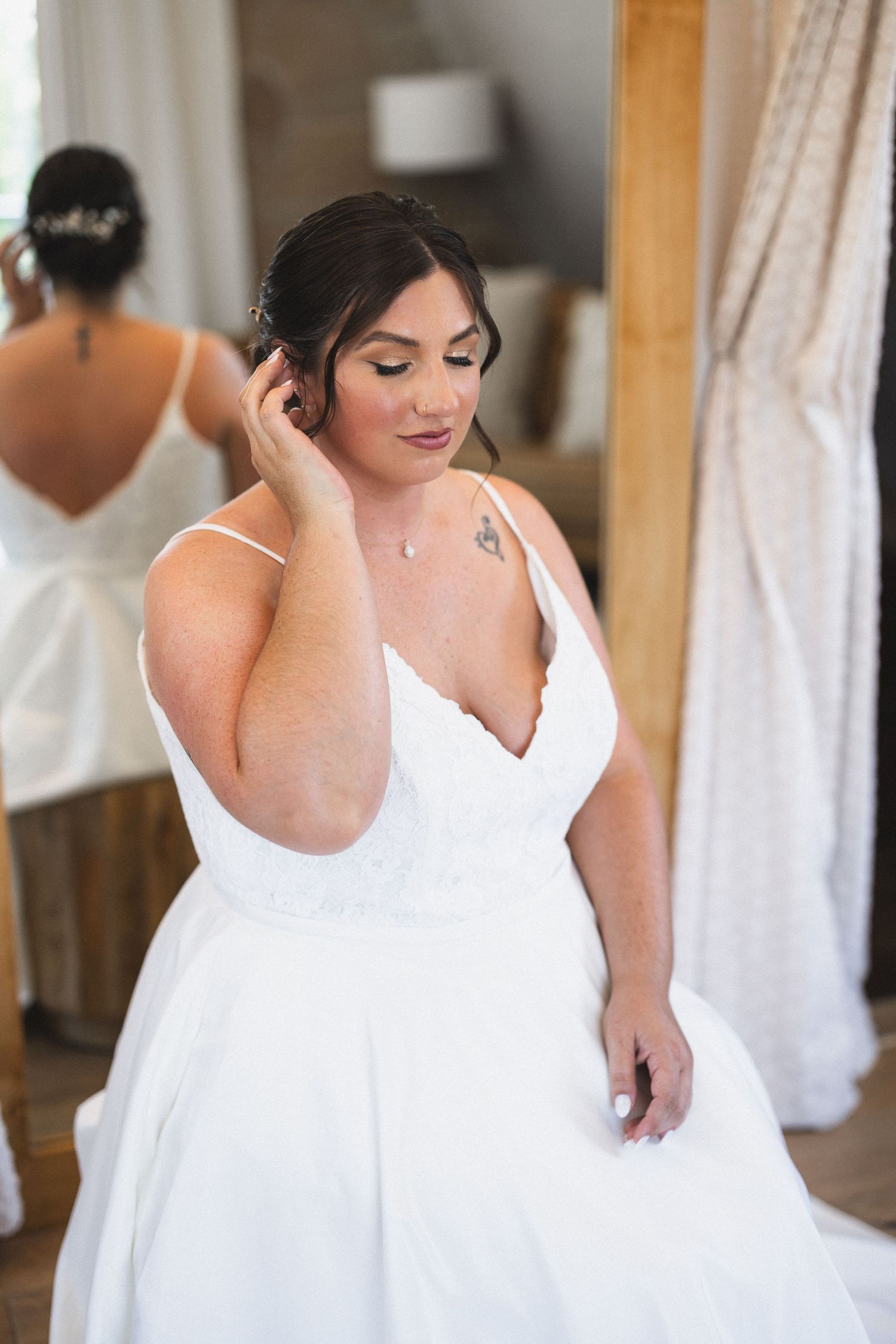 Bride in elegant white dress adjusting hair while standing near mirror.