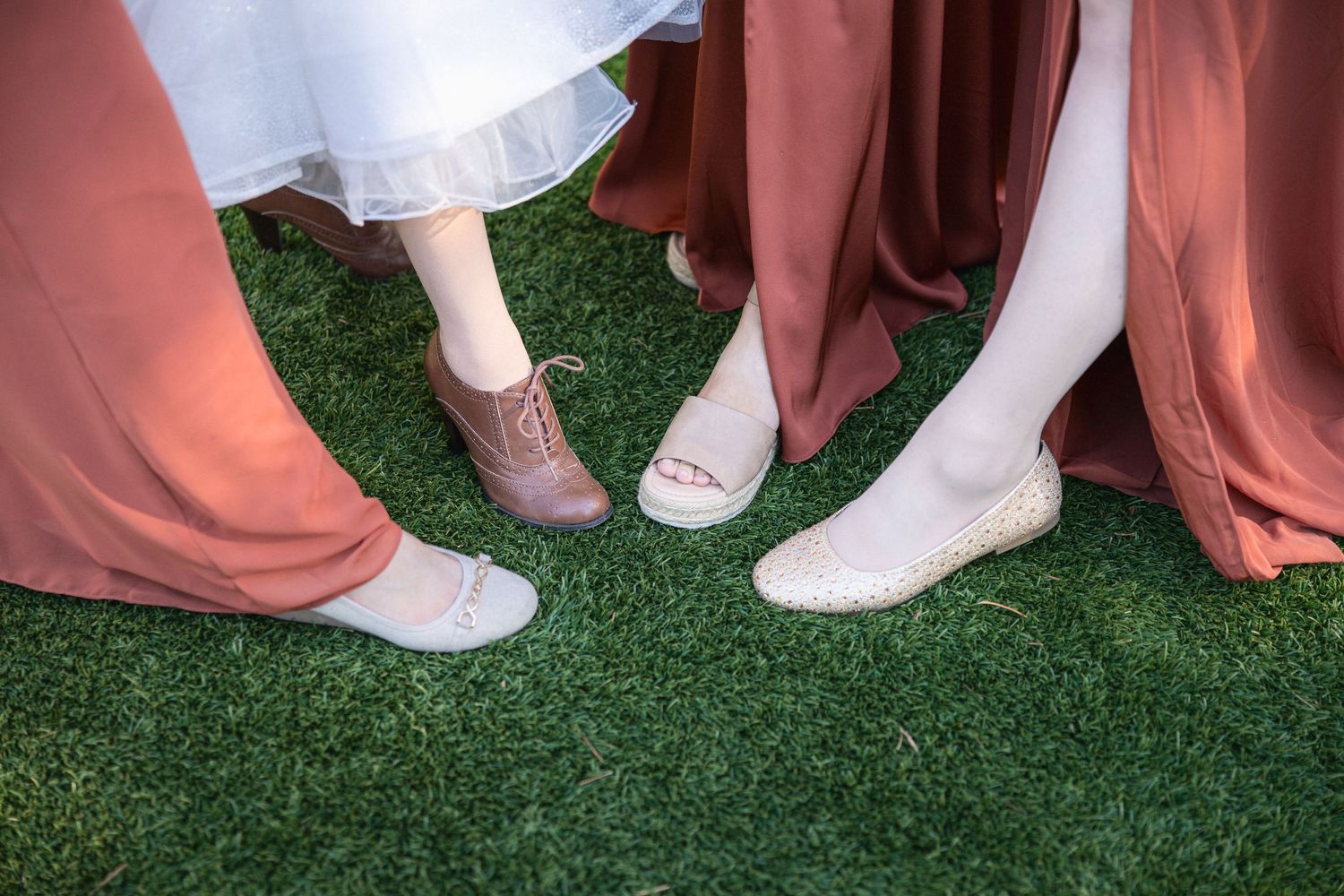 Detail shot of wedding party shoes showing contrast between formal footwear and casual boots on artificial grass.