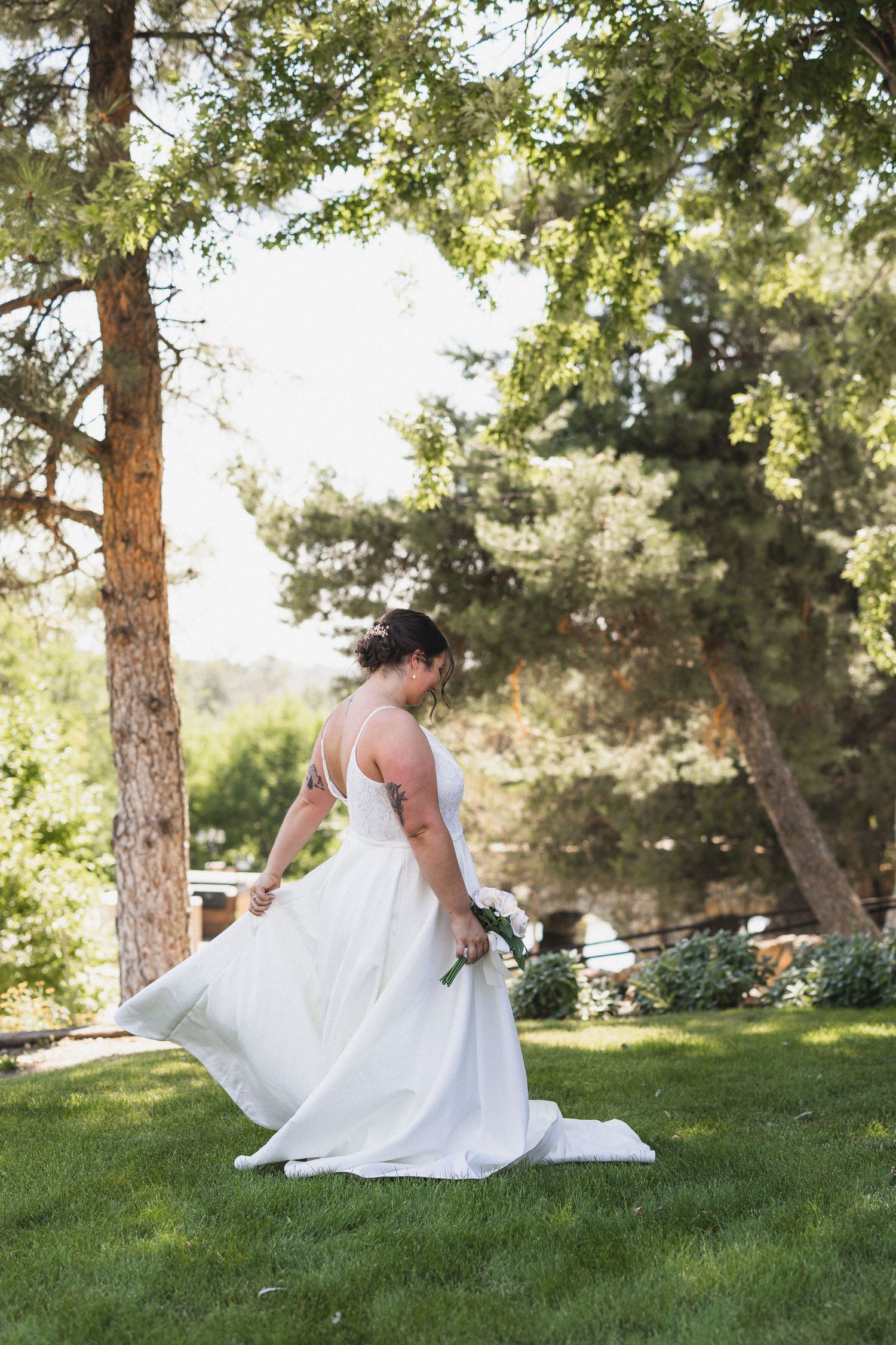 Bride in flowing white dress twirling in a sunlit garden setting.