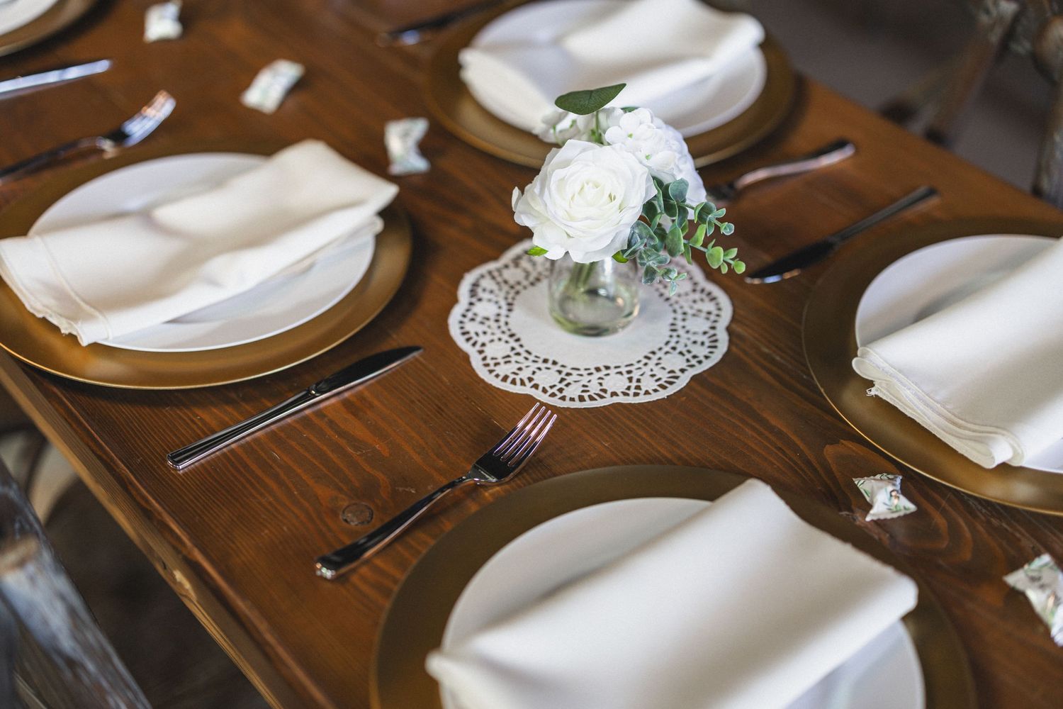 Wedding reception table with white napkins, gold chargers and small floral centerpieces.