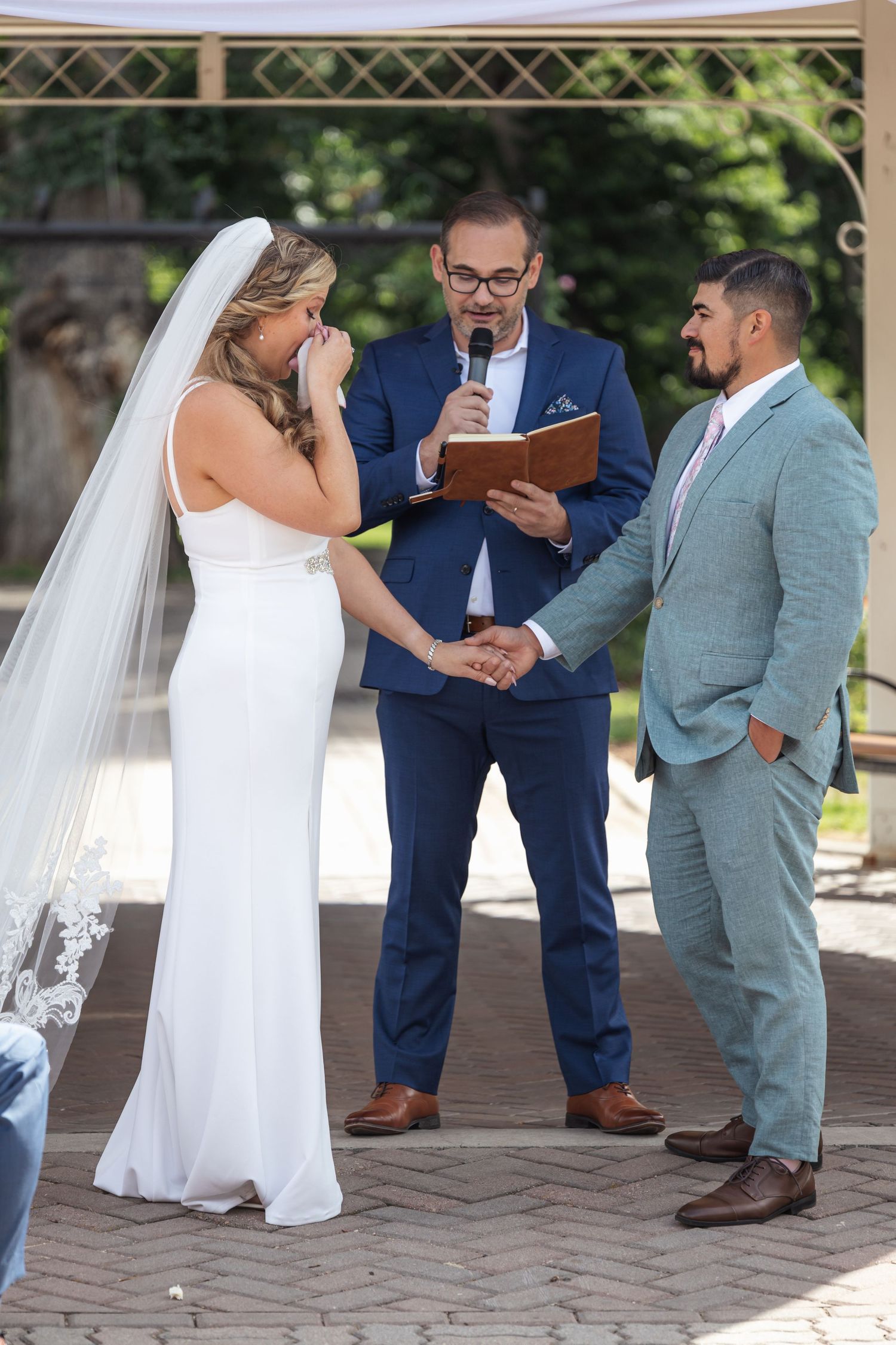 Wedding ceremony takes place under a gazebo with guests in formal attire.