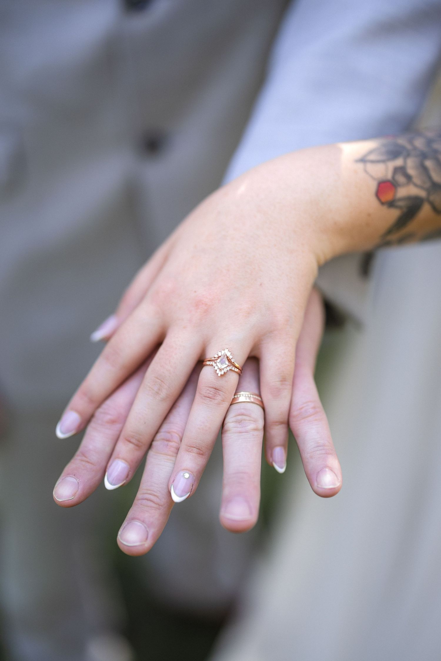 Close-up of engagement ring and tattooed hand with neutral manicure.