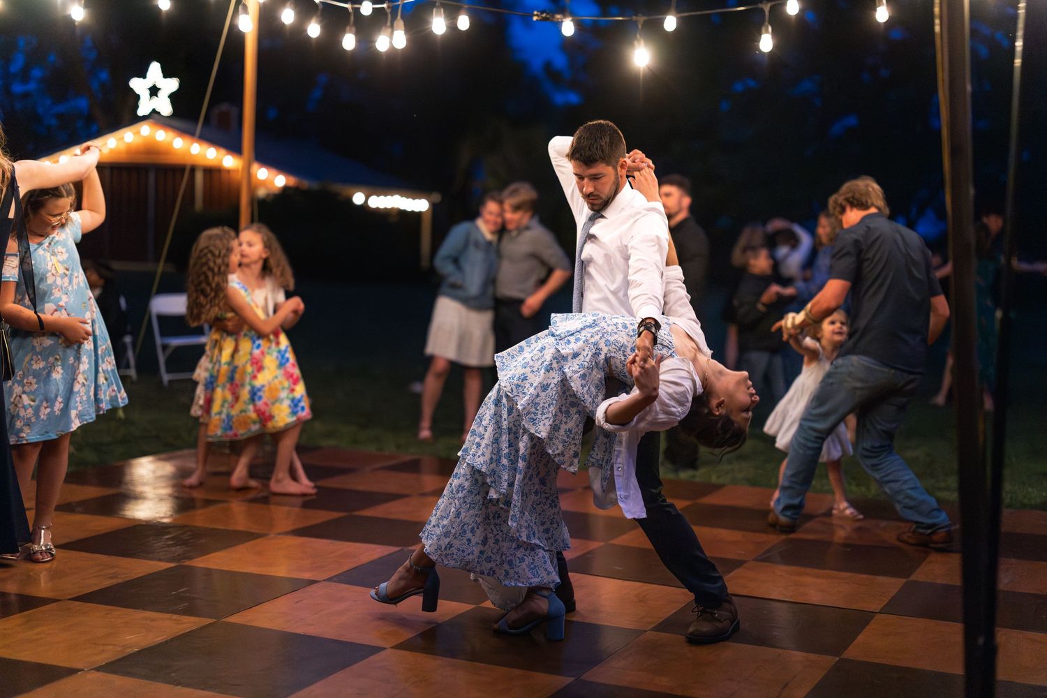 Couples dancing under twinkling lights during a joyful evening reception on an outdoor dance floor.