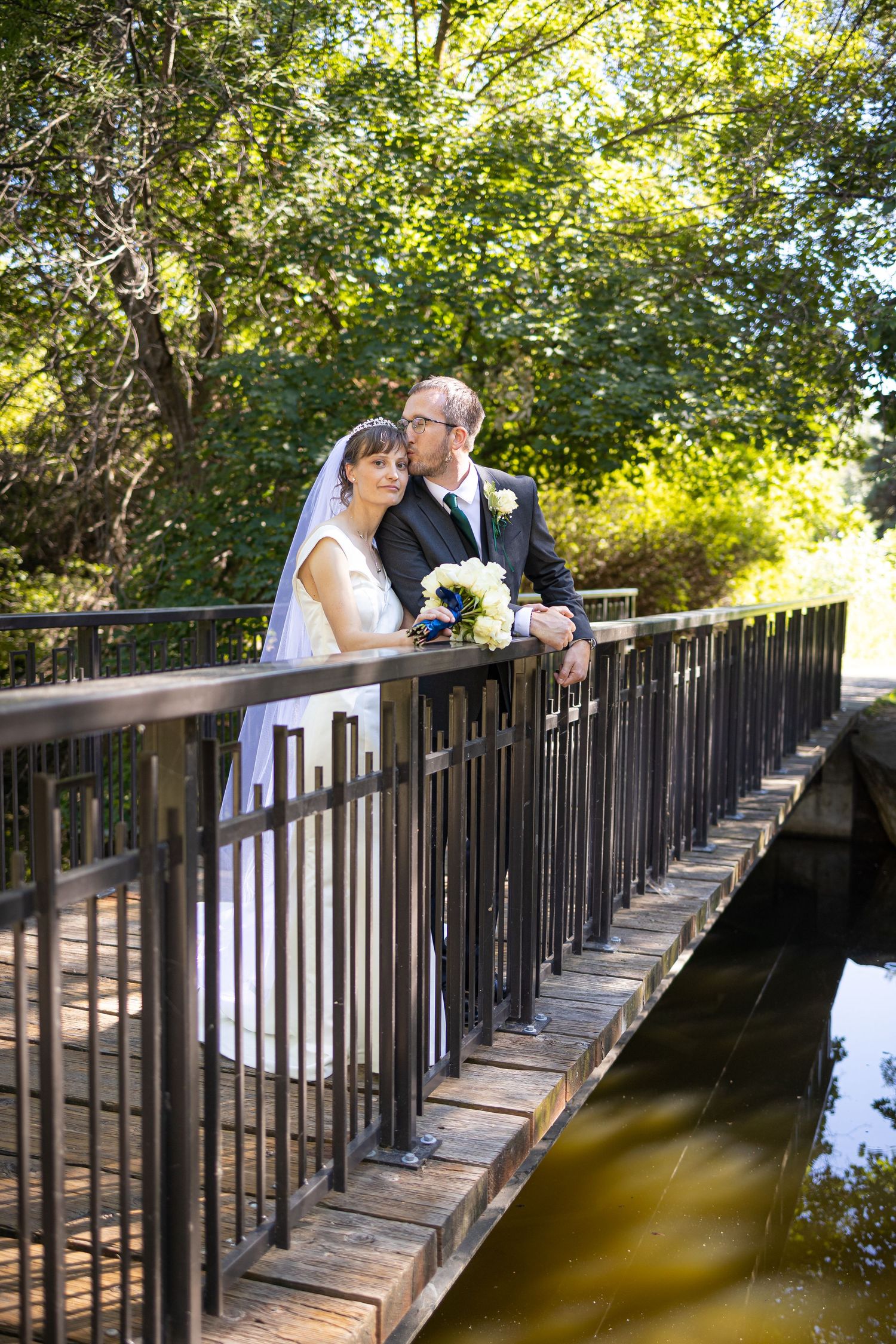 A couple shares an intimate moment on a wooden footbridge surrounded by lush greenery.