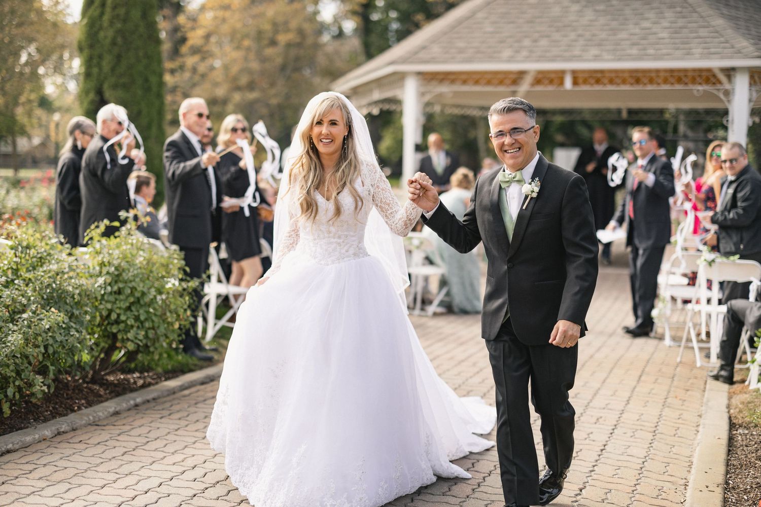 Wedding couple walks down brick path while guests applaud after ceremony.