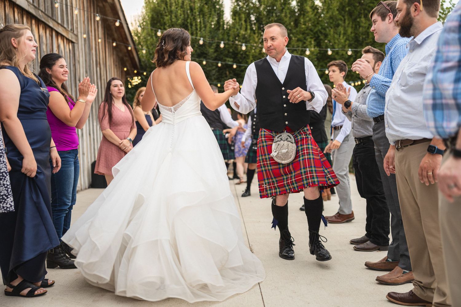 Wedding guests line up to watch dancing at an outdoor reception with string lights overhead.