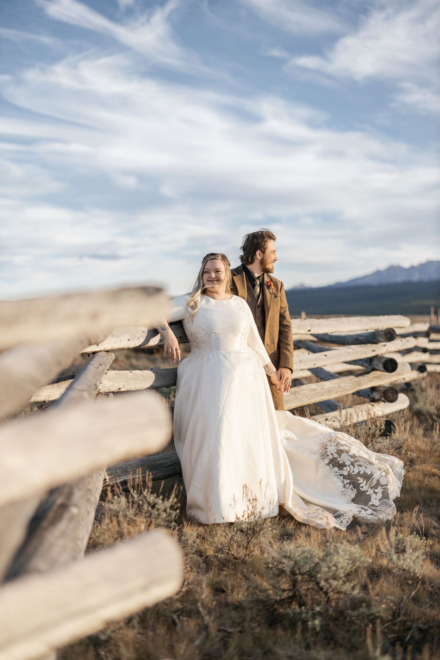 Newlyweds share an intimate moment on rocky terrain with mountains and dramatic sky in the background.