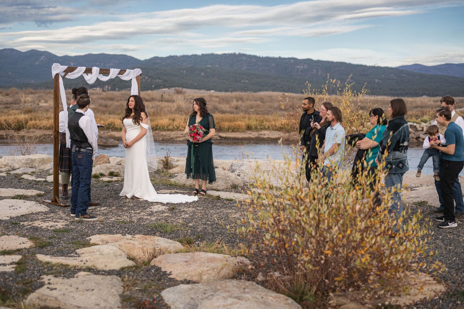 Intimate outdoor mountain wedding ceremony with wooden arch and natural lake backdrop.
