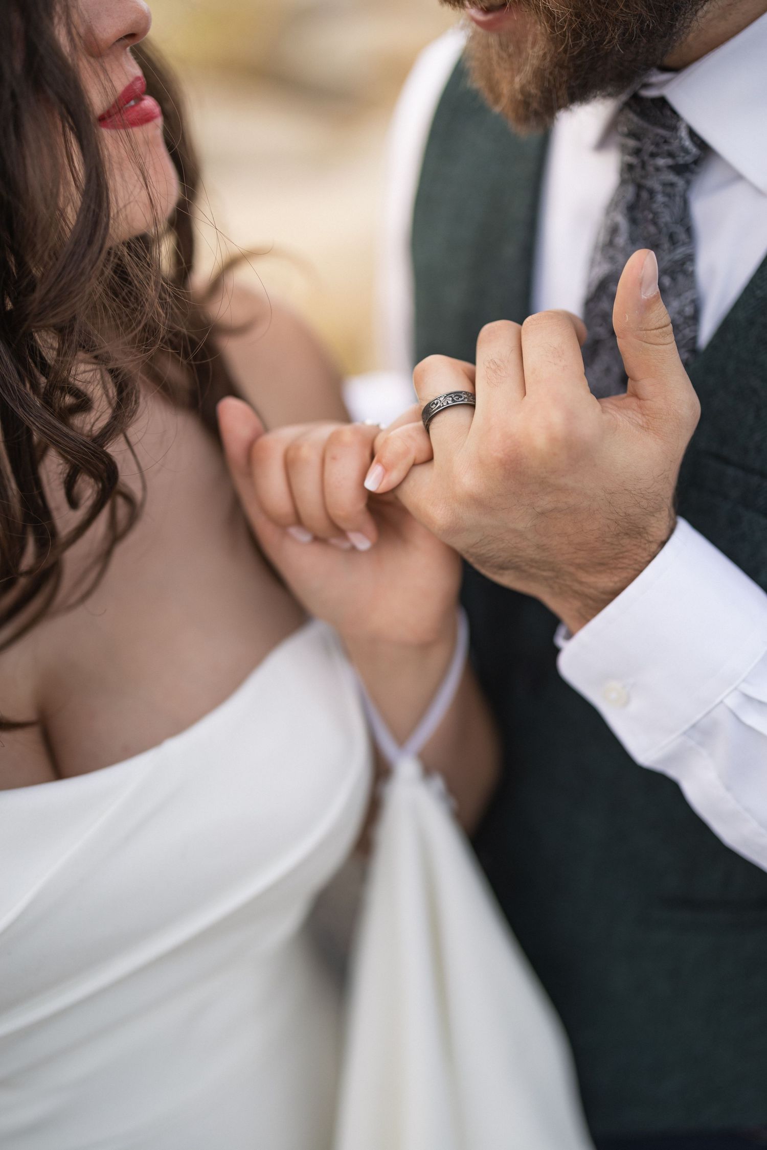 Intimate close-up of intertwined hands with wedding rings and white dress detail.