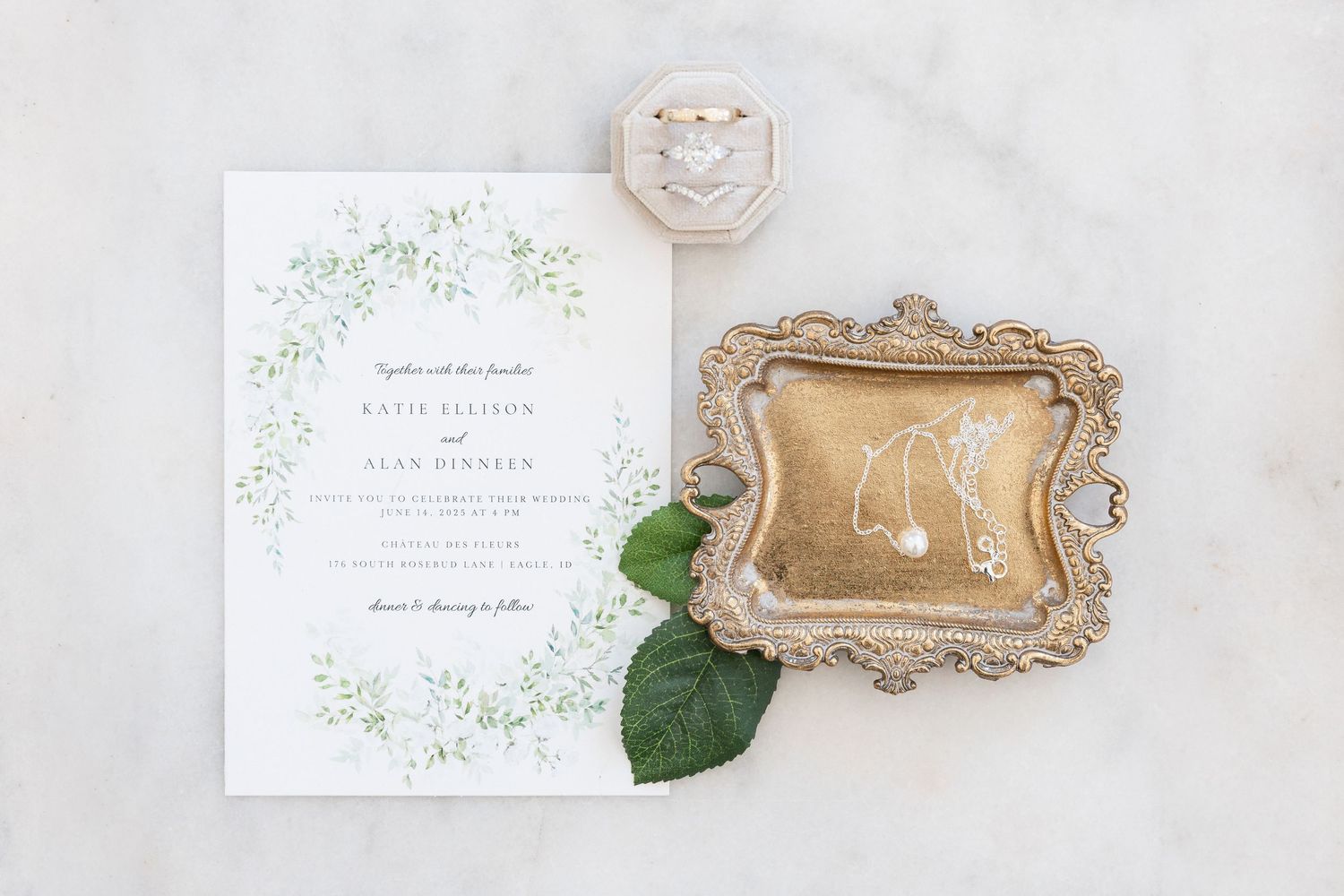 Wedding stationery with greenery design displayed alongside vintage gold tray and white roses on marble surface.
