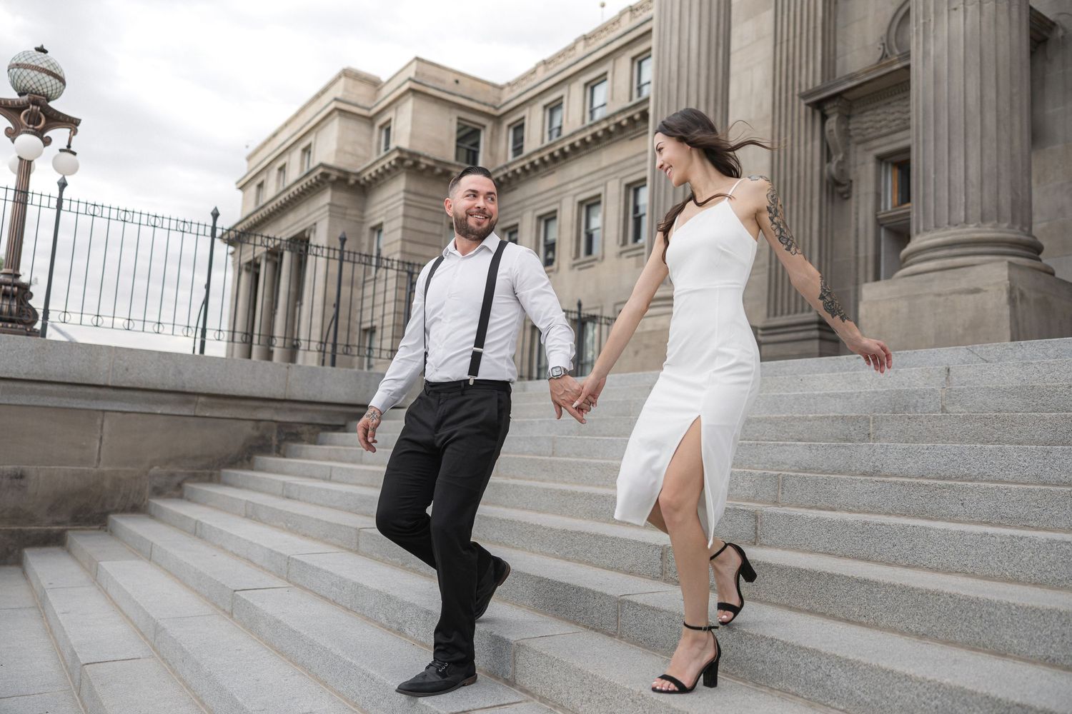 Two people perform dance moves on stone steps of a historic building facade.
