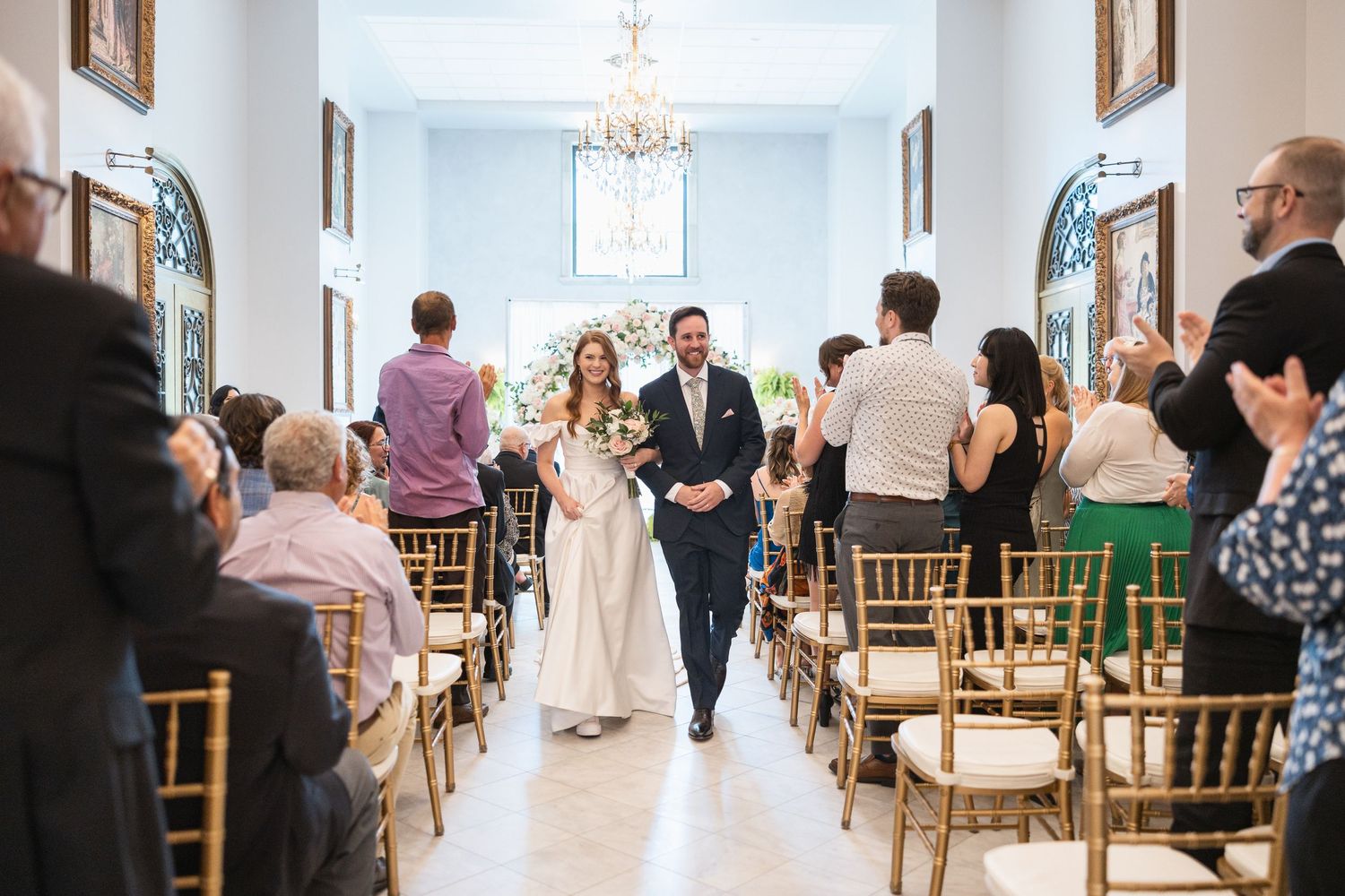 Panoramic view of a bright wedding chapel interior with wooden chairs and chandeliers.