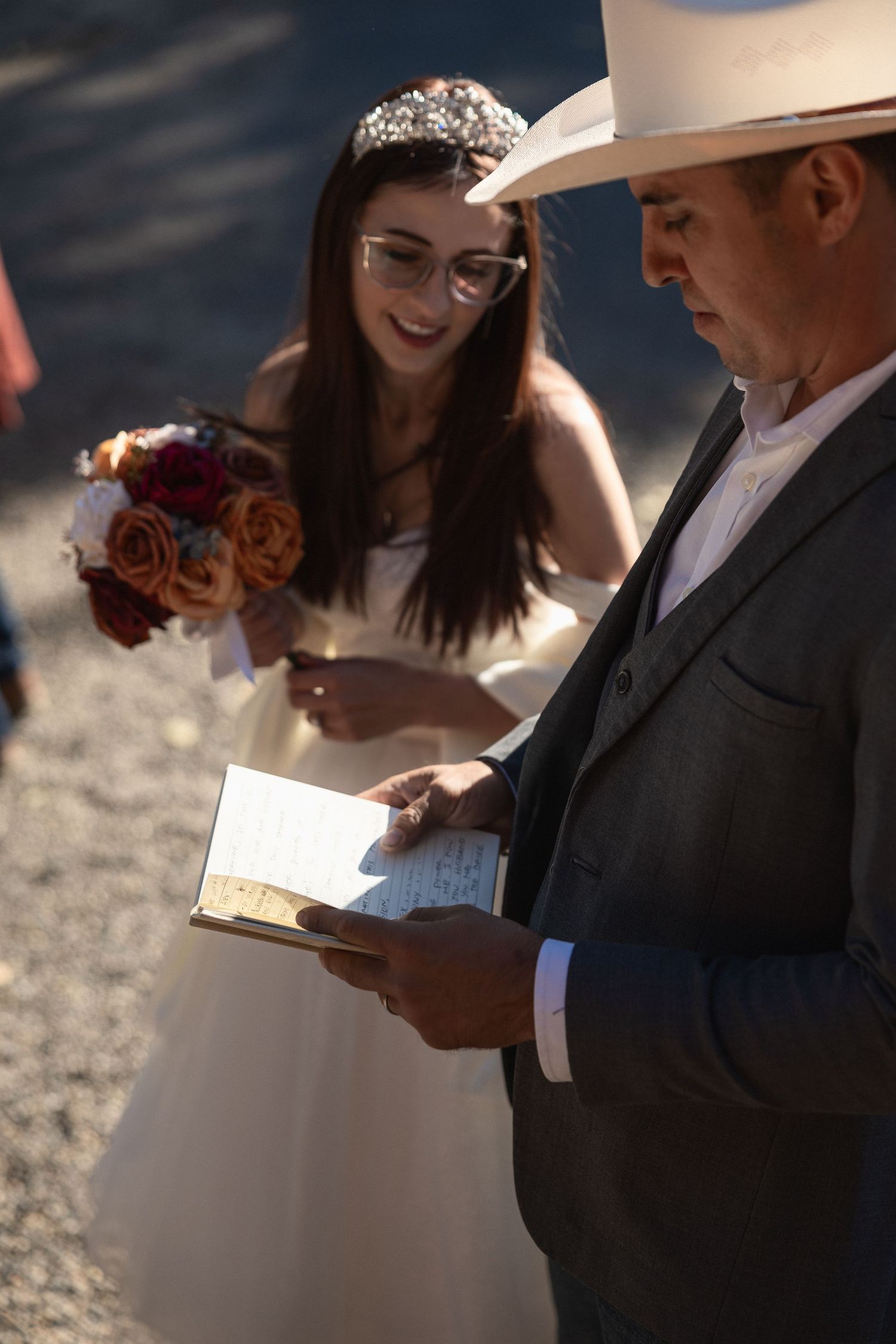 Wedding ceremony participants reading from books during an outdoor service.