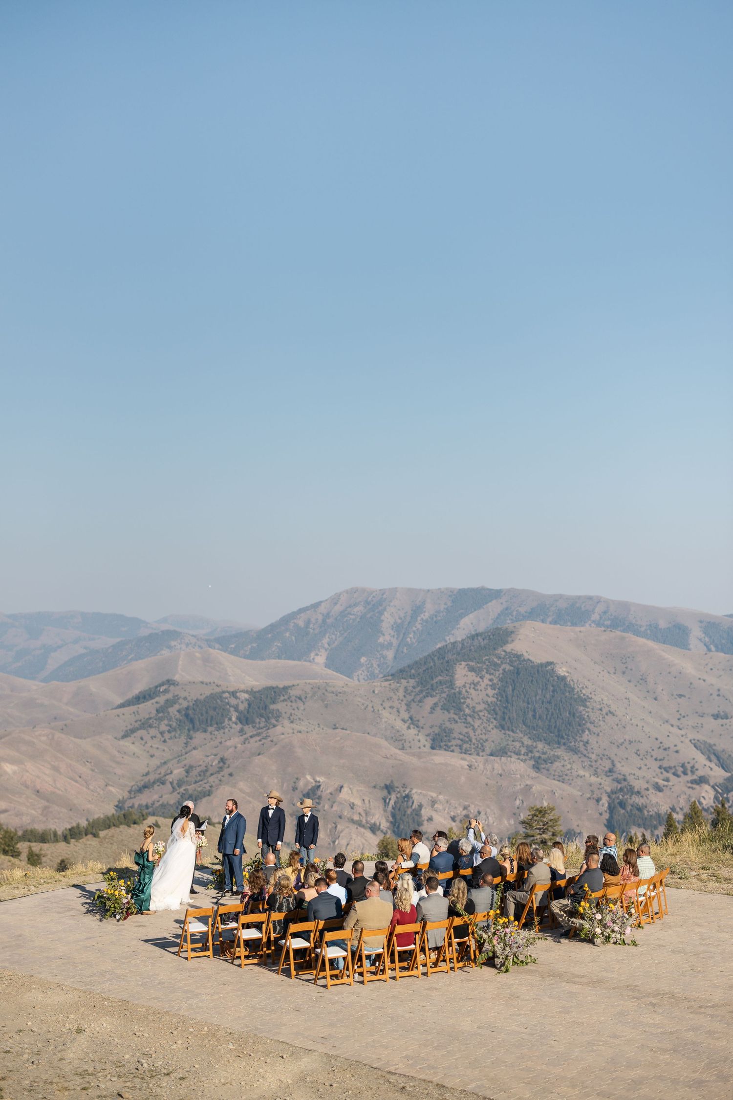 Panoramic mountain wedding ceremony setup with wooden chairs arranged in rows against a backdrop of rugged peaks.