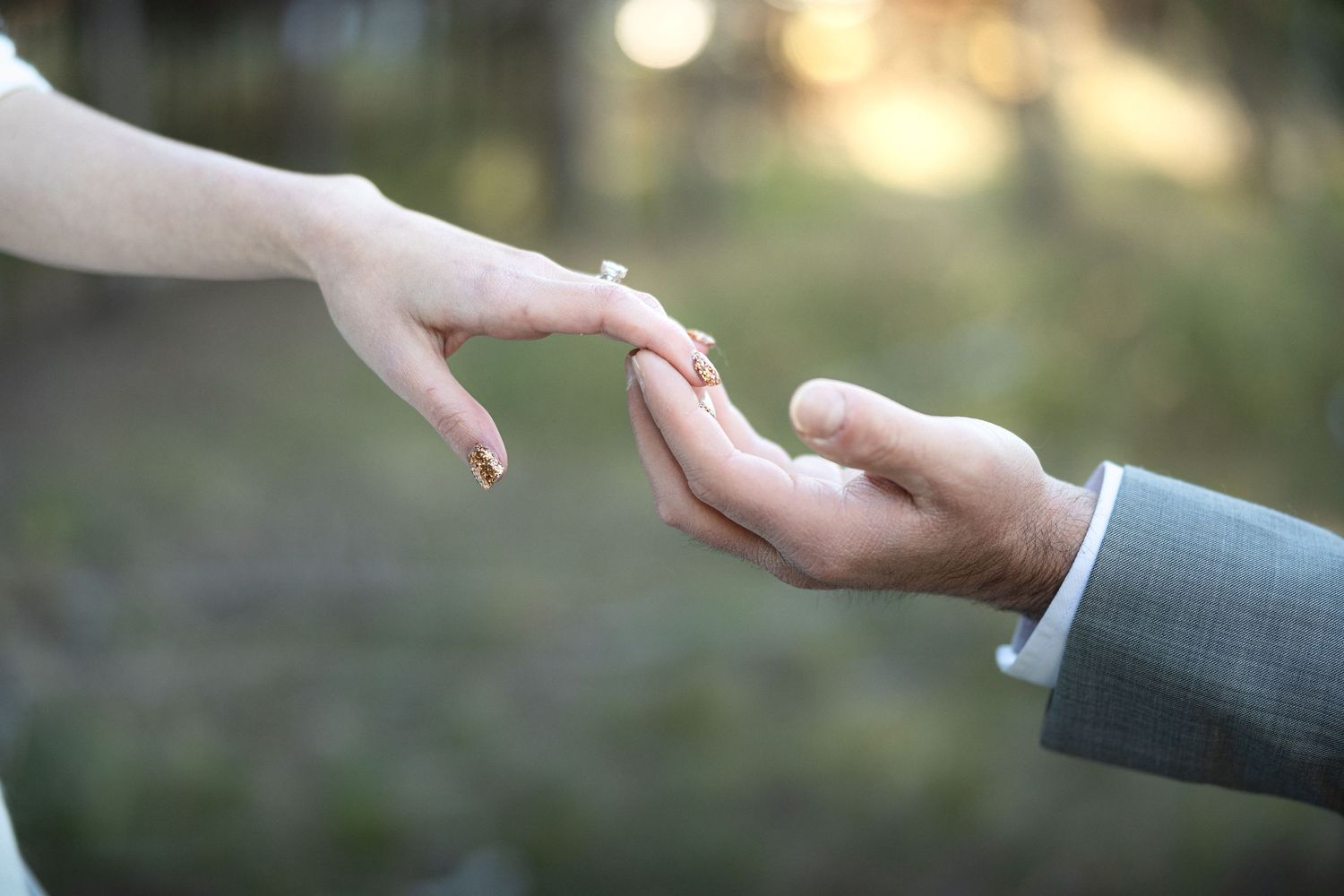 Romantic close-up of hands reaching toward each other during outdoor wedding ceremony.