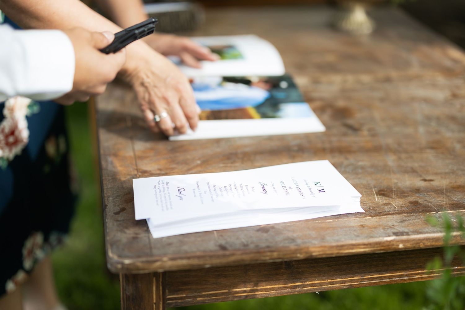 Hands signing papers on a rustic wooden surface during an event.