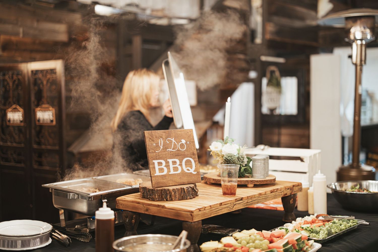 BBQ station with rising steam at wedding reception buffet featuring wooden decor.