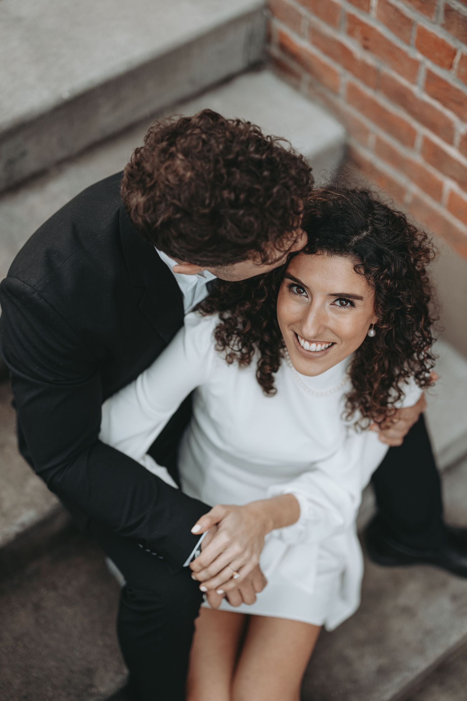 An intimate portrait of a couple in black and white attire against brick wall.