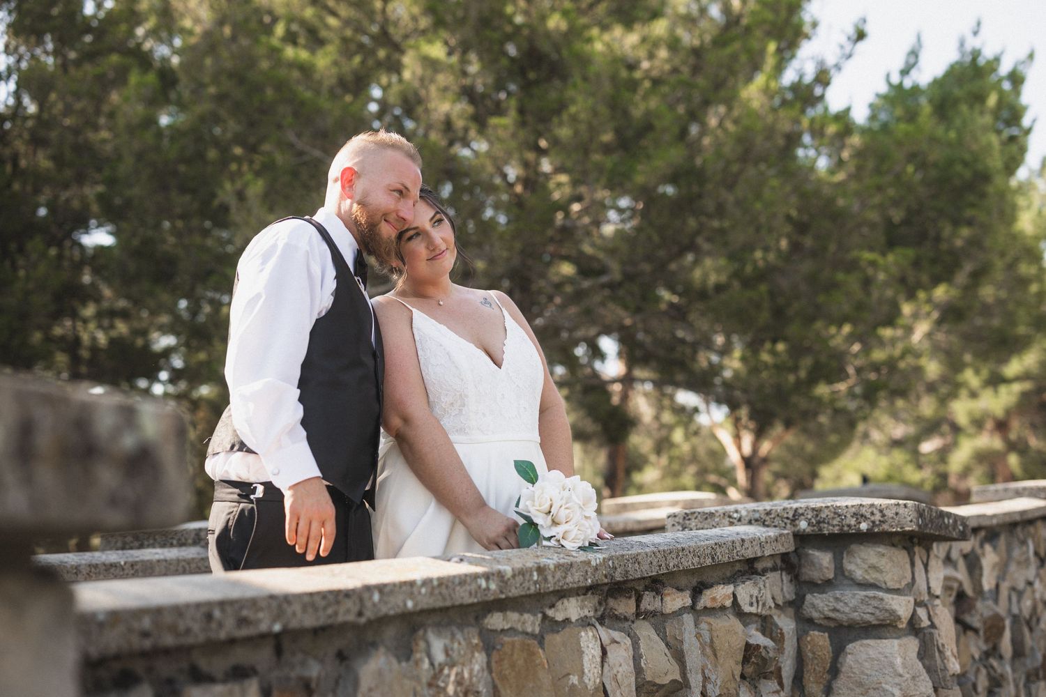 Romantic wedding couple shares intimate moment on stone wall during outdoor photo session.