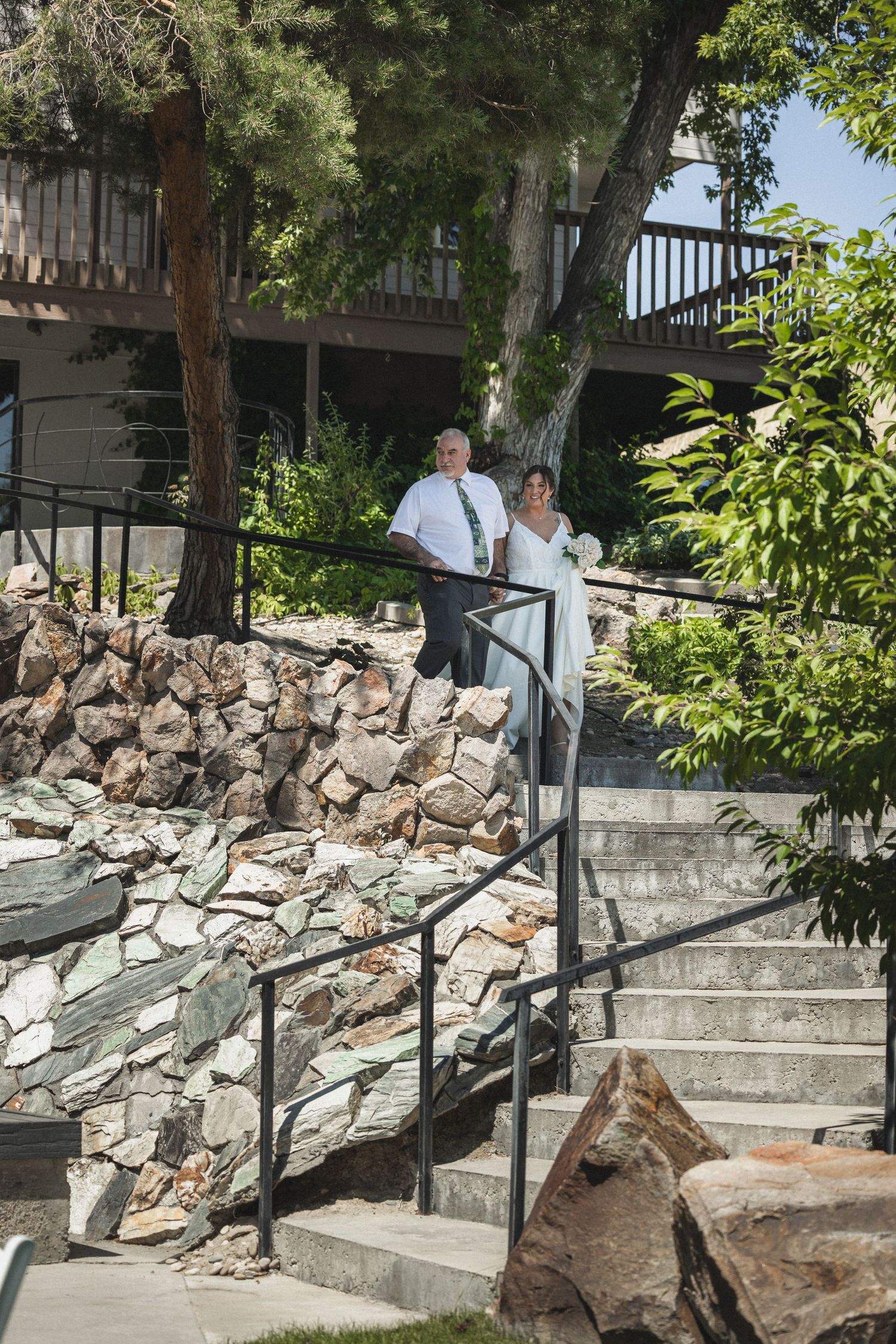 A couple and officiant descend stone steps at an outdoor wedding venue.