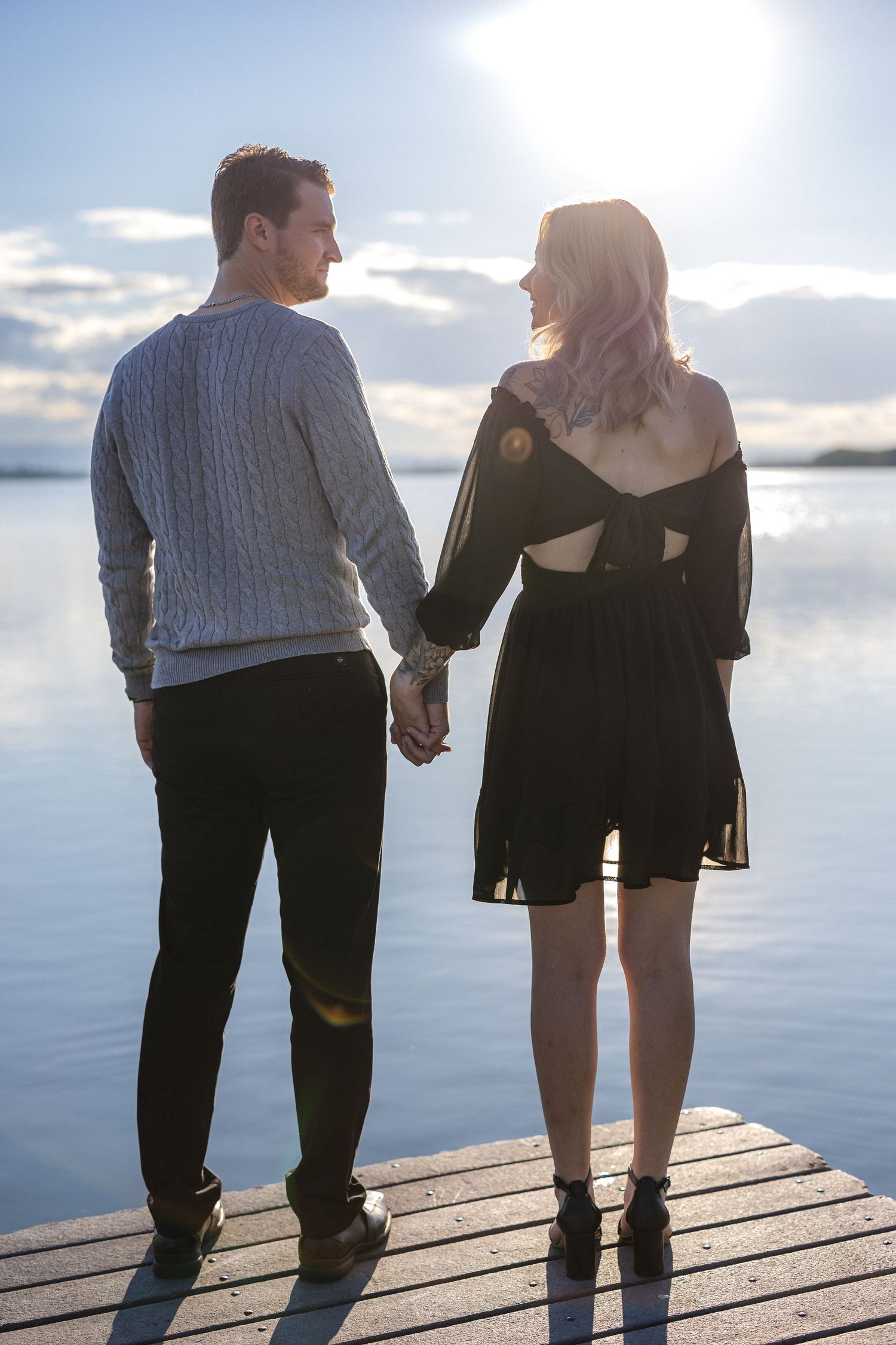 Romantic couple holding hands on a wooden dock at sunset by a serene lake.