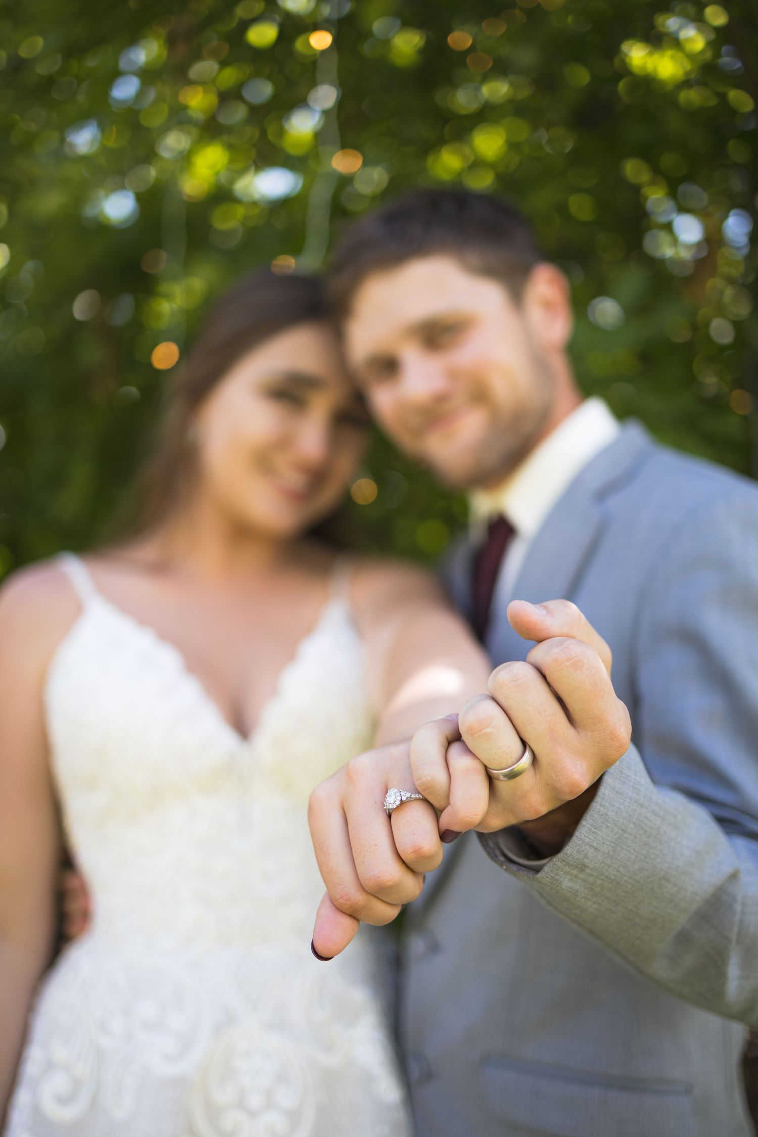 Close-up shot of newlyweds' hands with wedding rings against a blurred garden background.