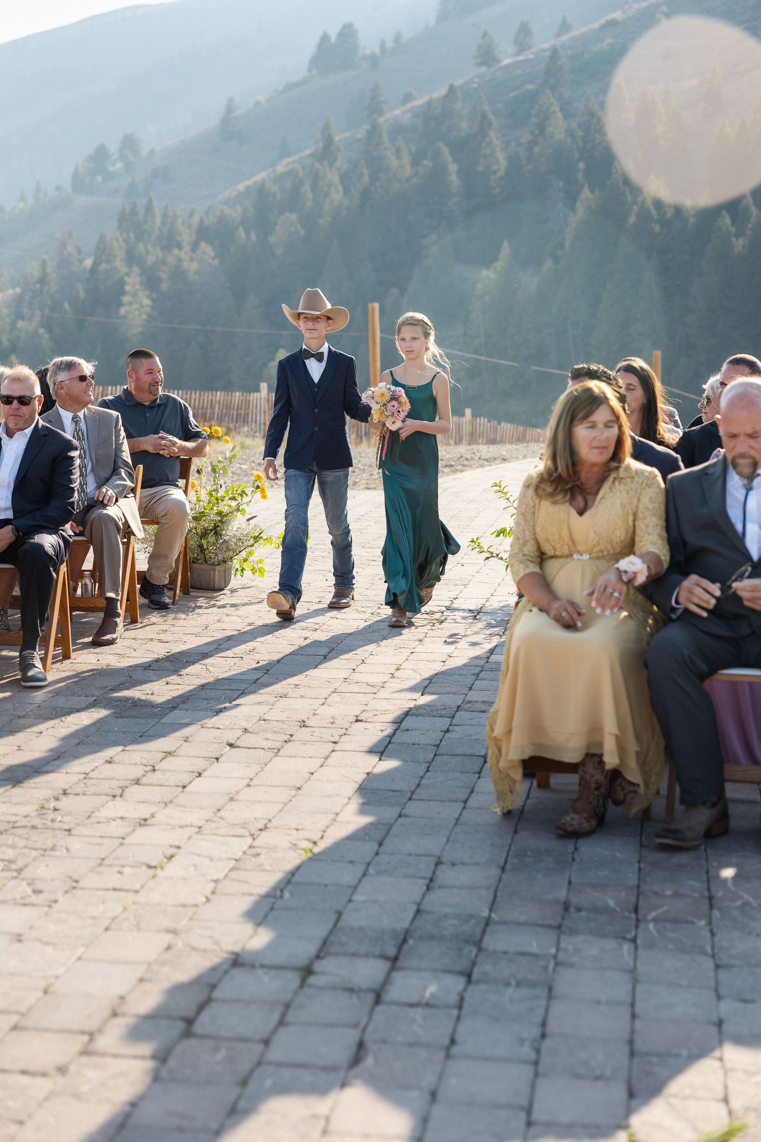 Wedding ceremony setup on a mountain path with guests seated and scenic mountain views.
