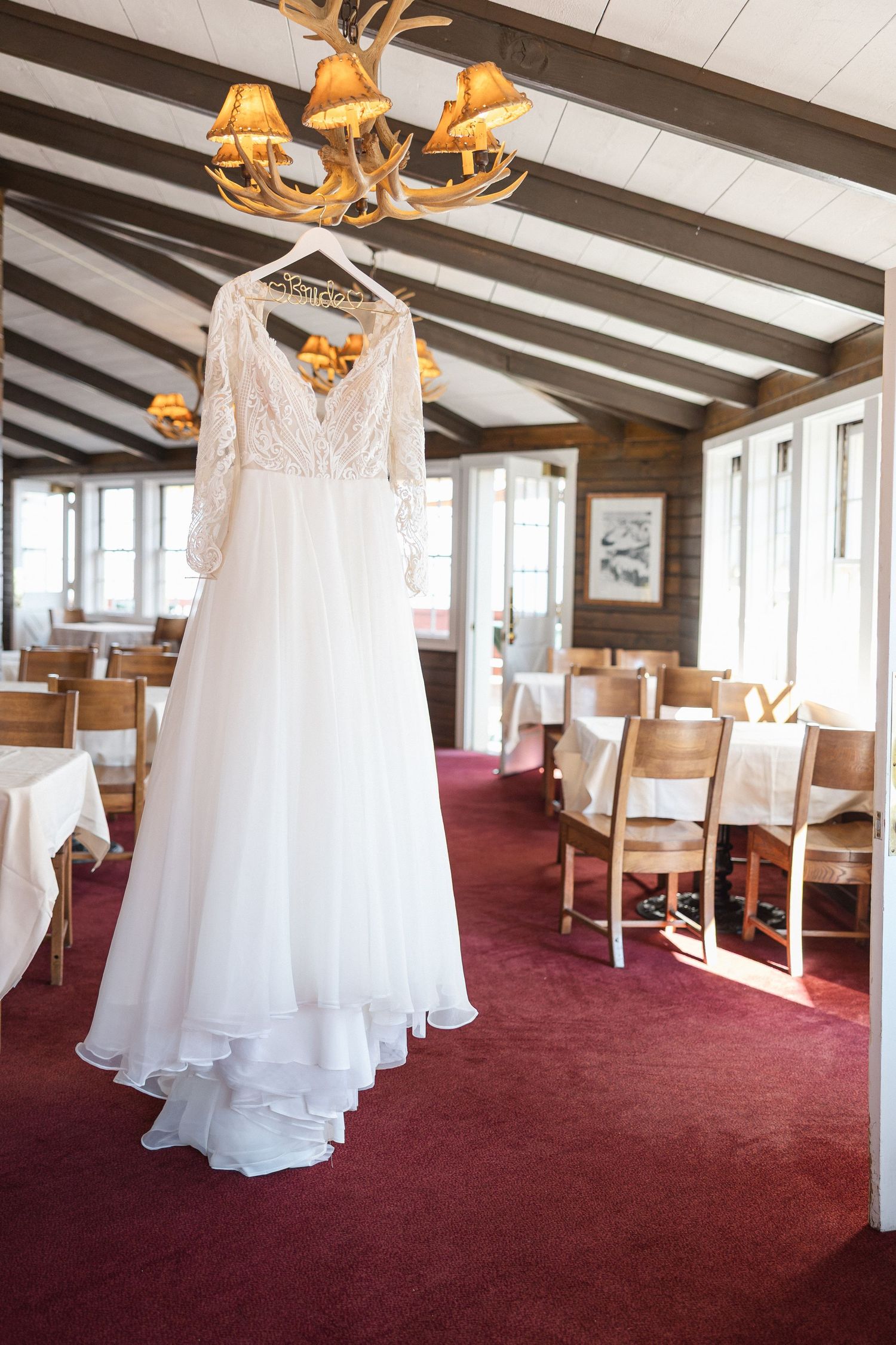 White wedding dress hanging in a rustic venue with exposed wooden beams and red carpeting.