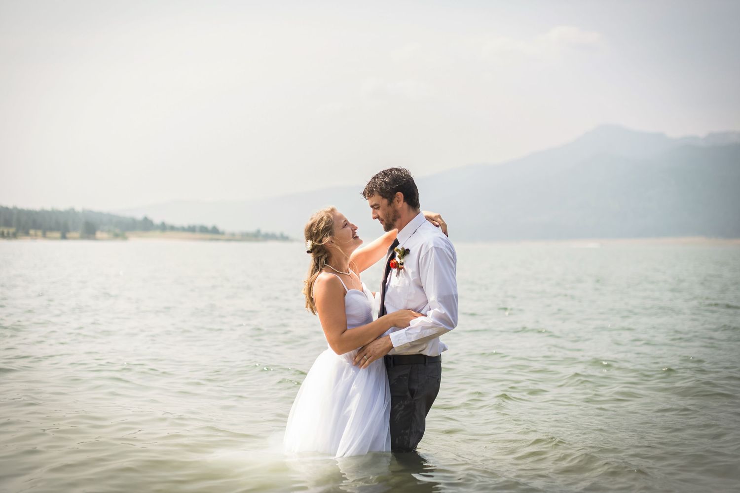 Newlyweds sharing an intimate moment while standing in lake water with mountains behind them.