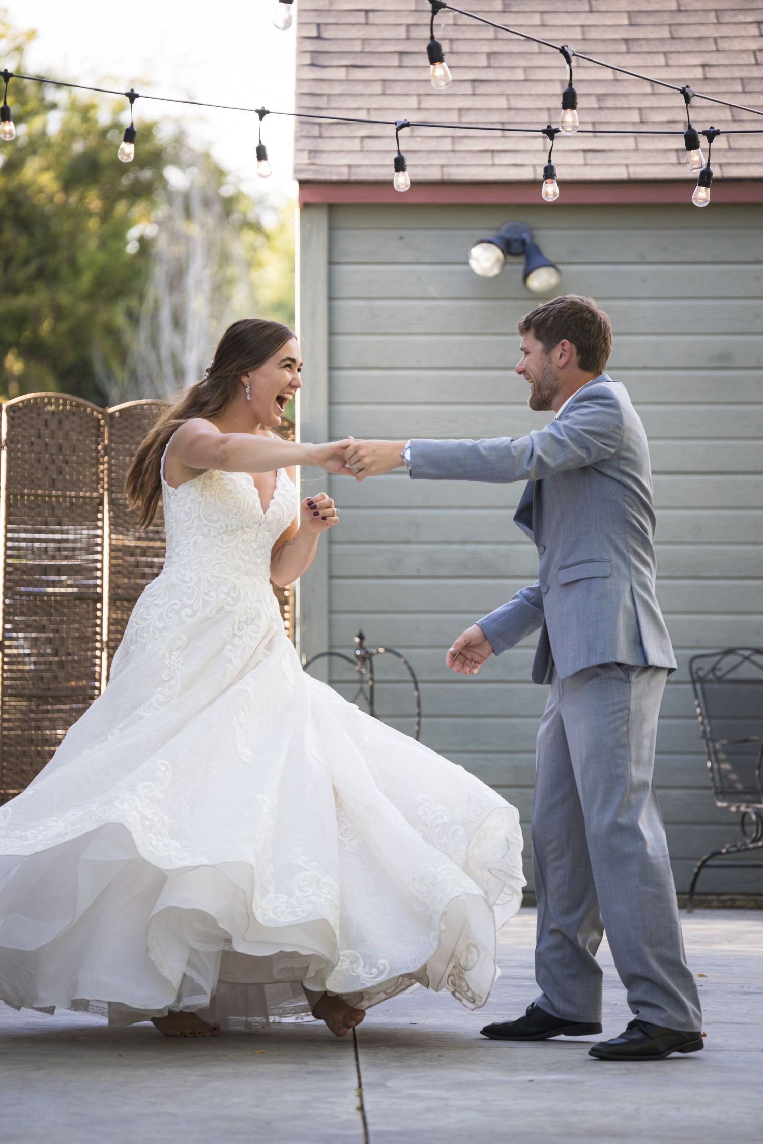 A couple dances joyfully on an outdoor patio during their wedding celebration.