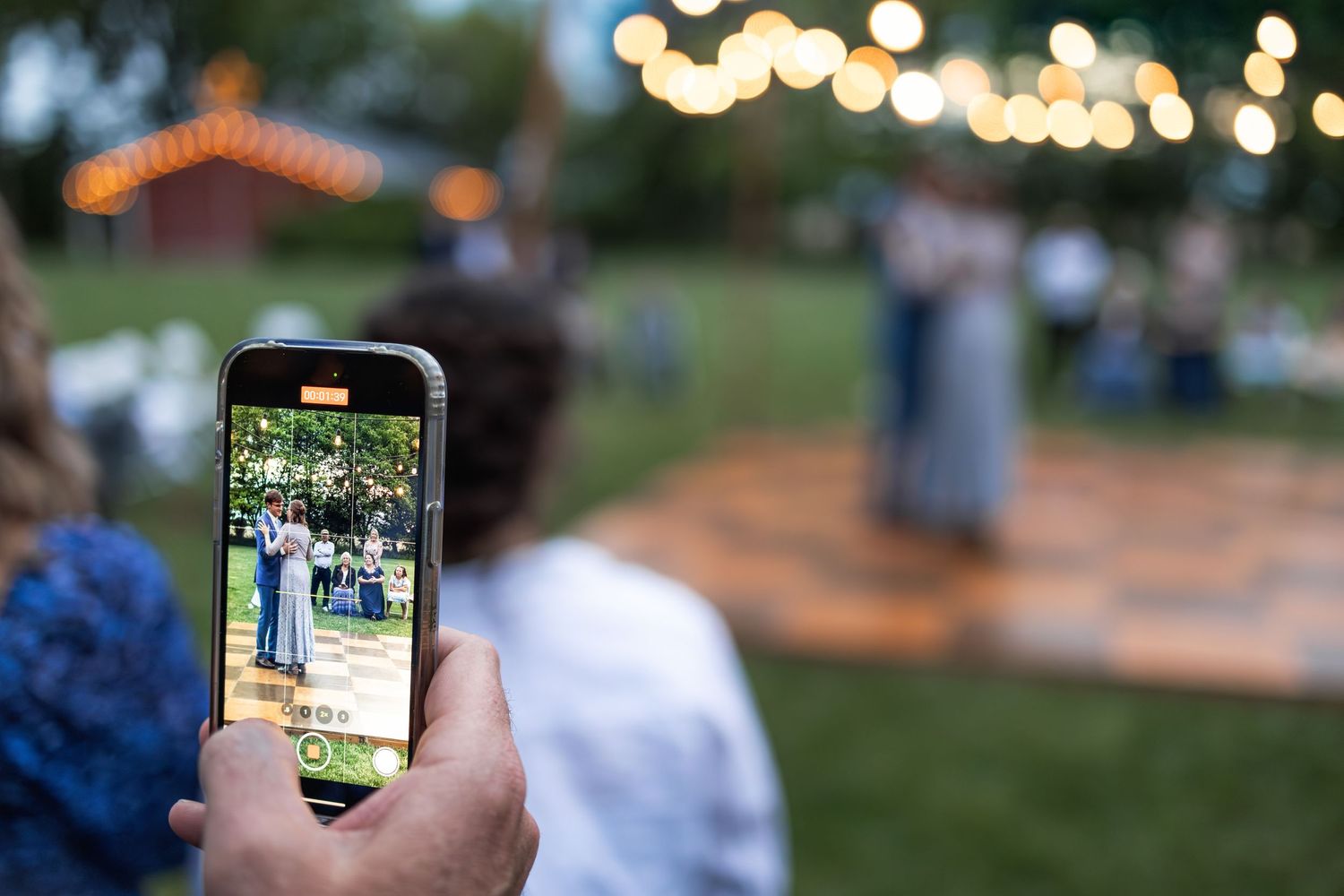 Someone captures a wedding dance moment through their smartphone at an outdoor reception.