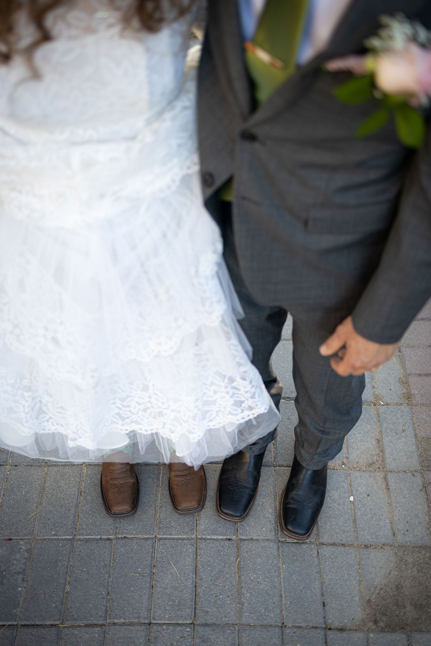 Close-up of bride and groom's feet on stone pavement, showing wedding attire details.