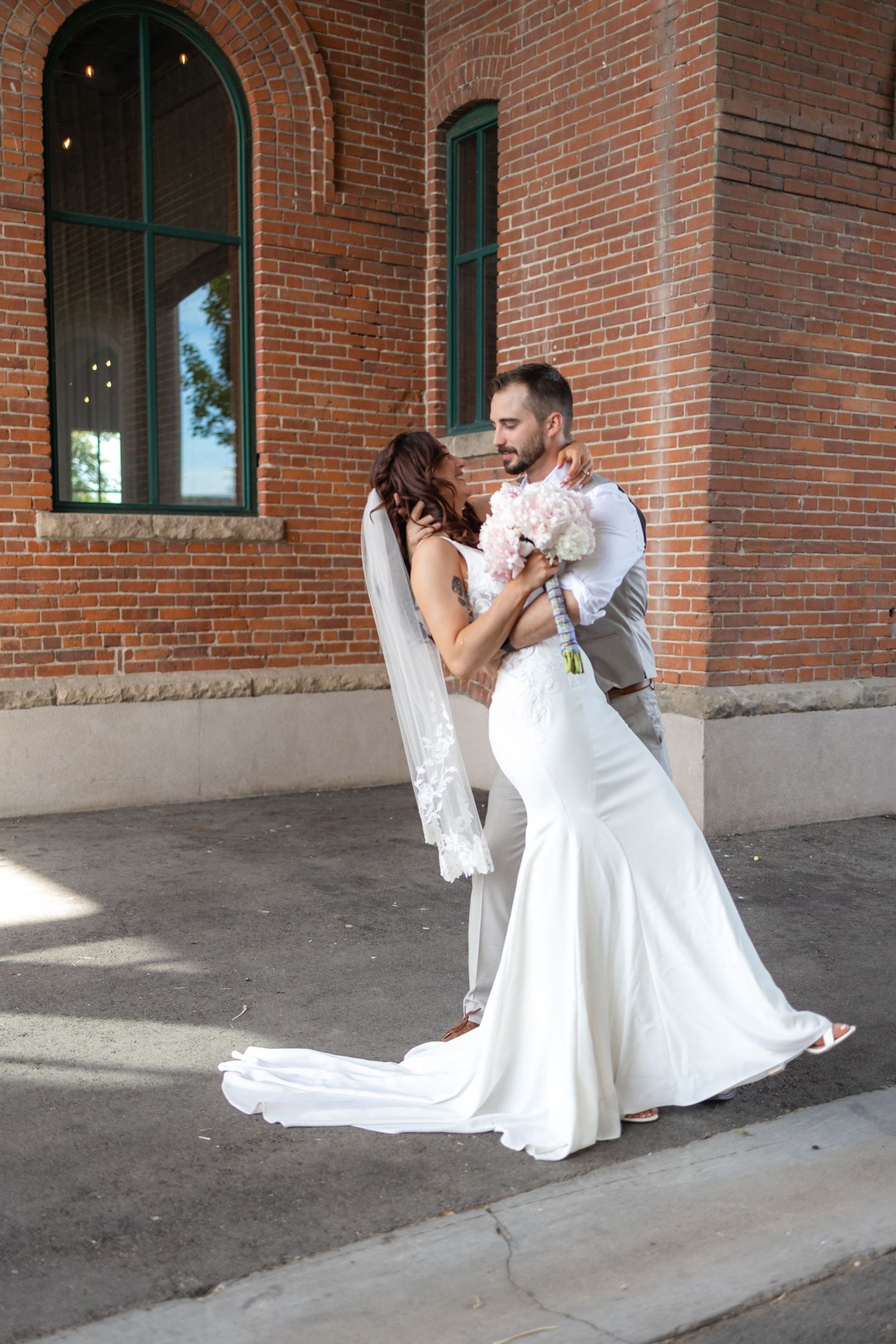 Newlyweds share a romantic dance pose in front of a historic brick building.