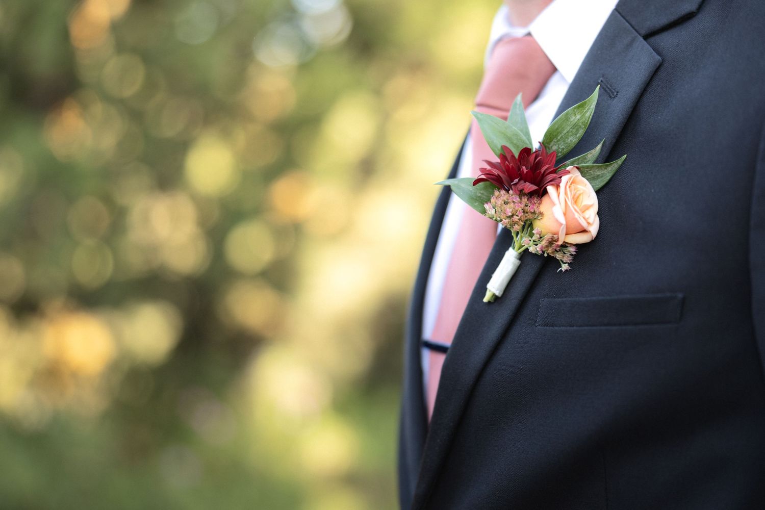 Close-up detail of groomsmen's black suit jackets with pink boutonnières.