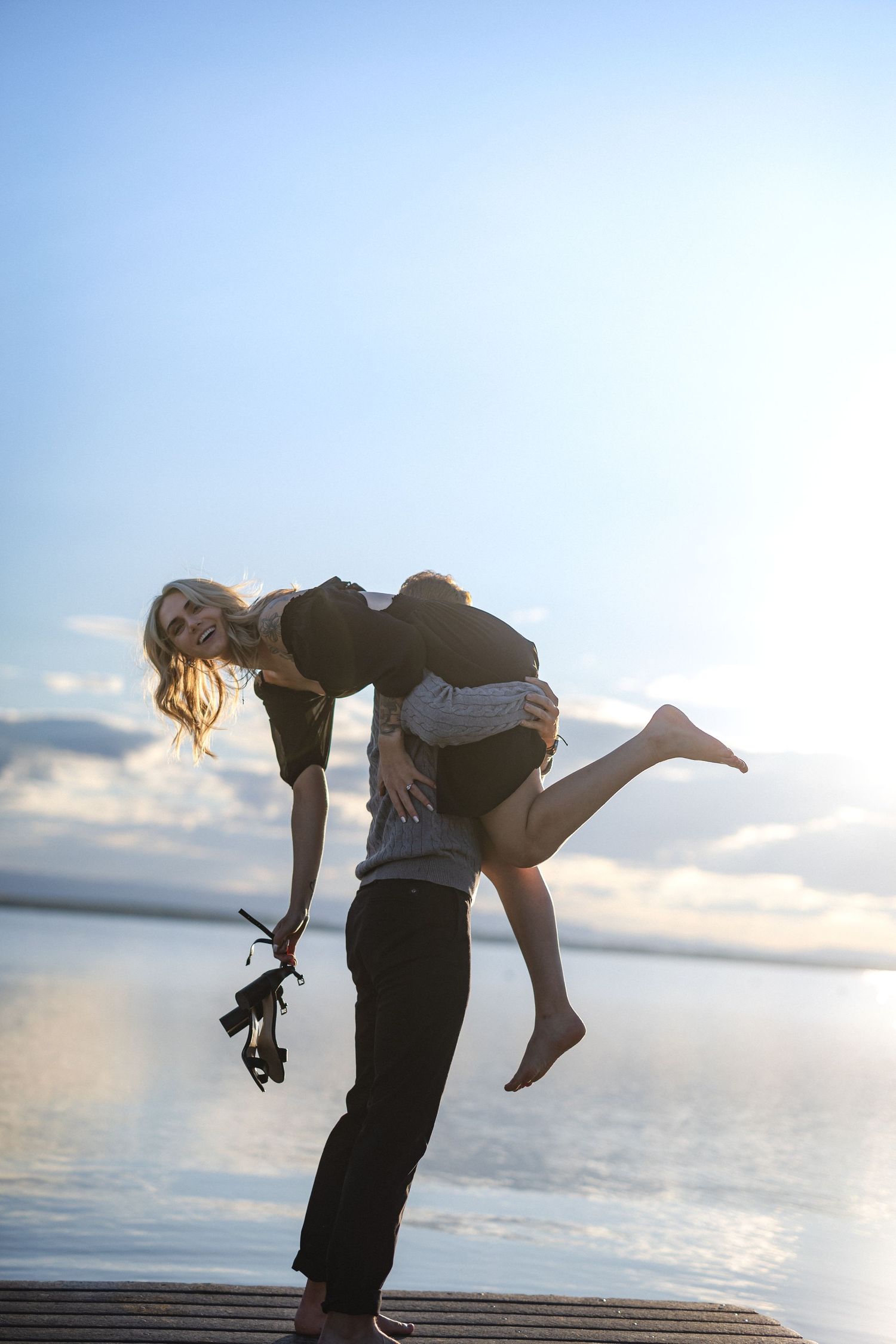 Silhouetted figures dance and dip on a dock against a sunset sky.