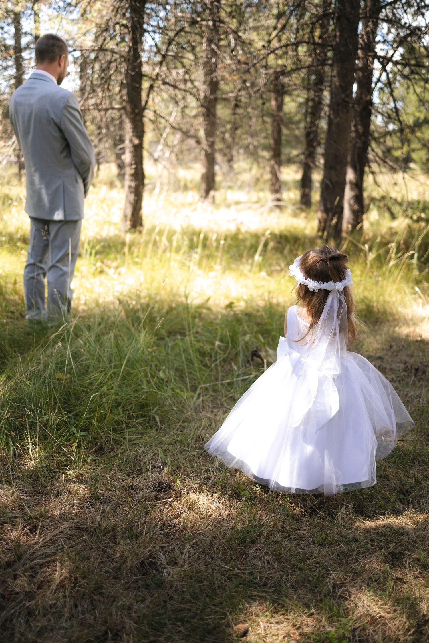 Touching wedding moment with flower girl watching groom in sunlit forest.