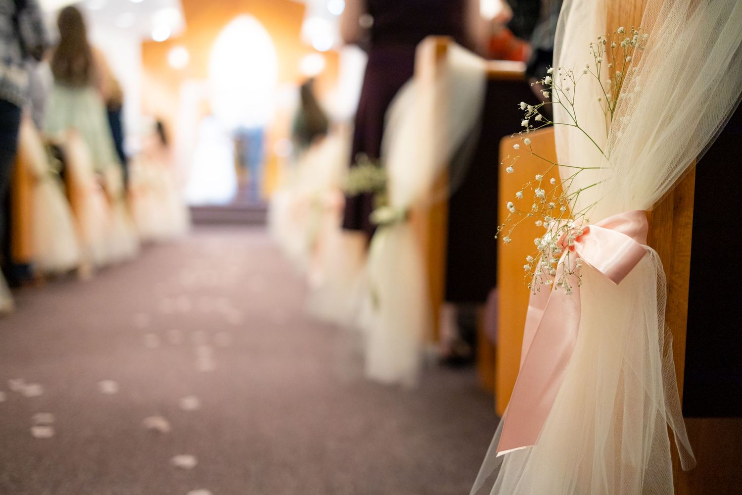 Close-up of white tulle and flower decorations on church pews.