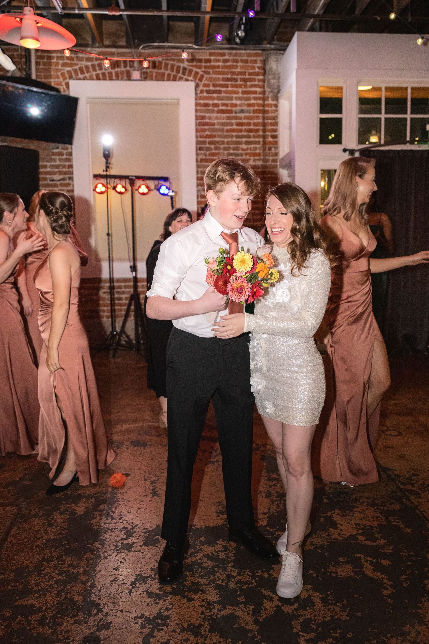 Wedding reception guests dancing and celebrating on a rustic dance floor with brick walls.