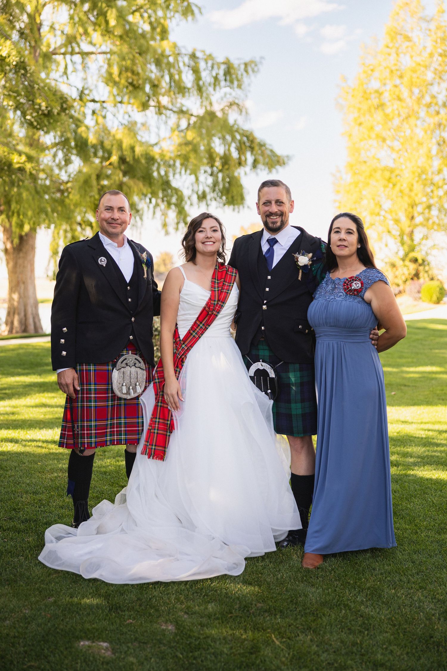 Wedding party poses outdoors in Scottish and formal attire on a sunny day.
