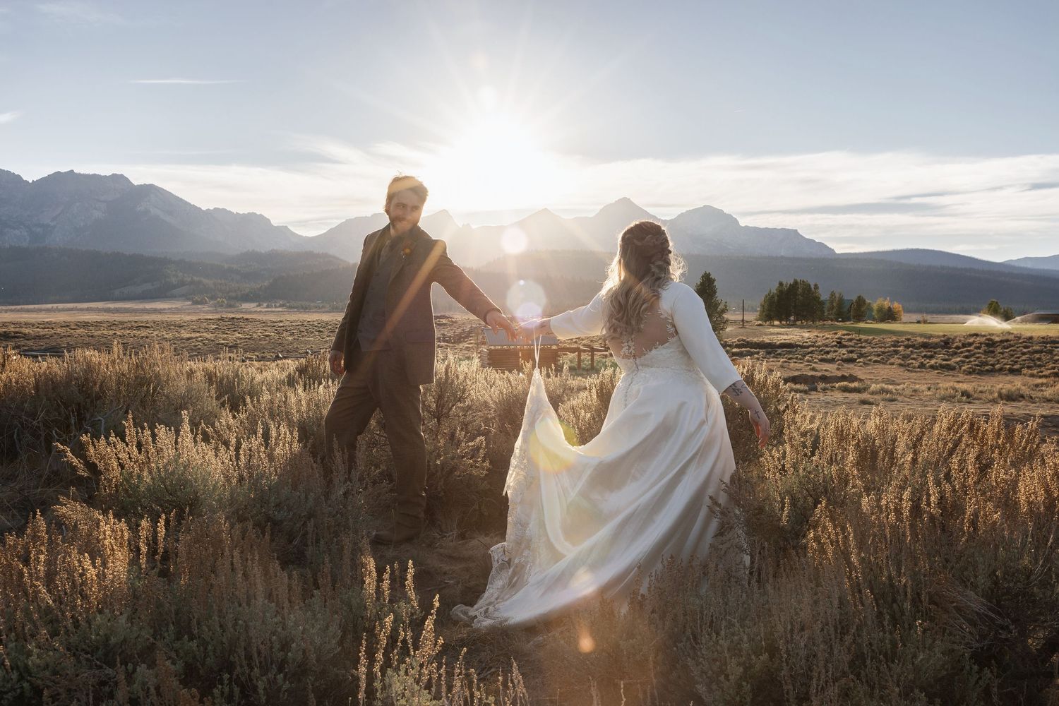 Wedding couple embracing in a scenic mountain field at sunset with dramatic lighting and flowing veil.
