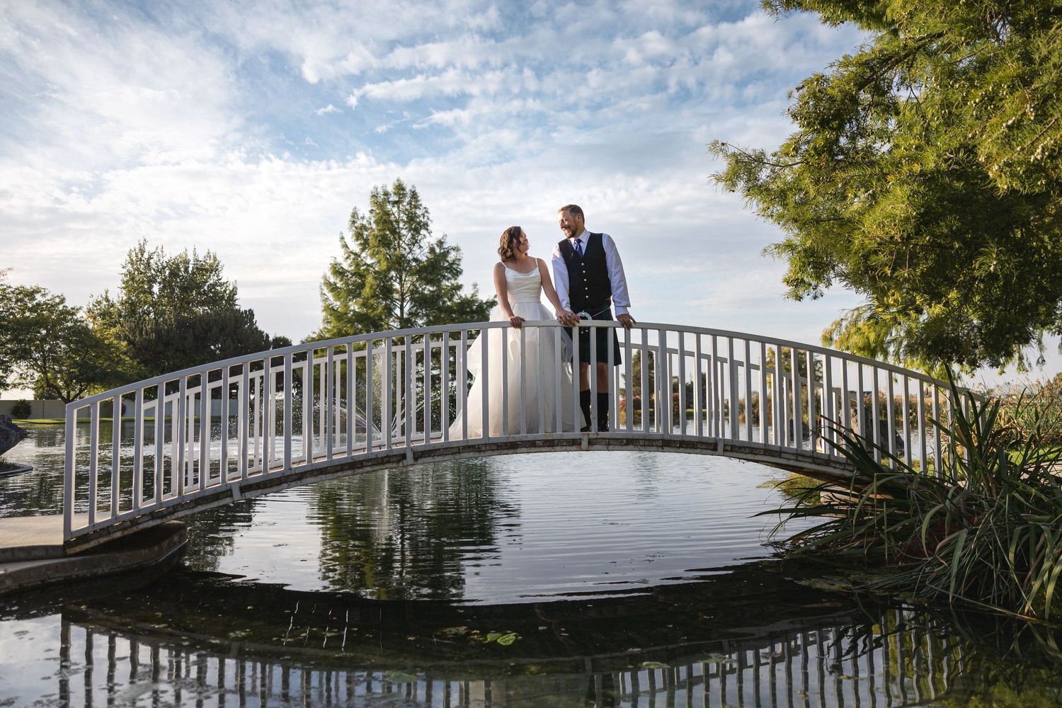 A couple stands on an arched bridge over reflective water during their wedding celebration.