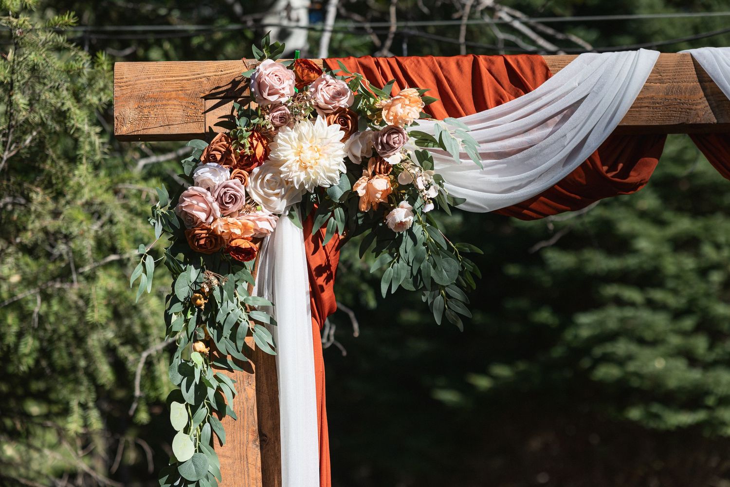 White draped fabric with floral arrangements decorating an outdoor wedding ceremony arch.