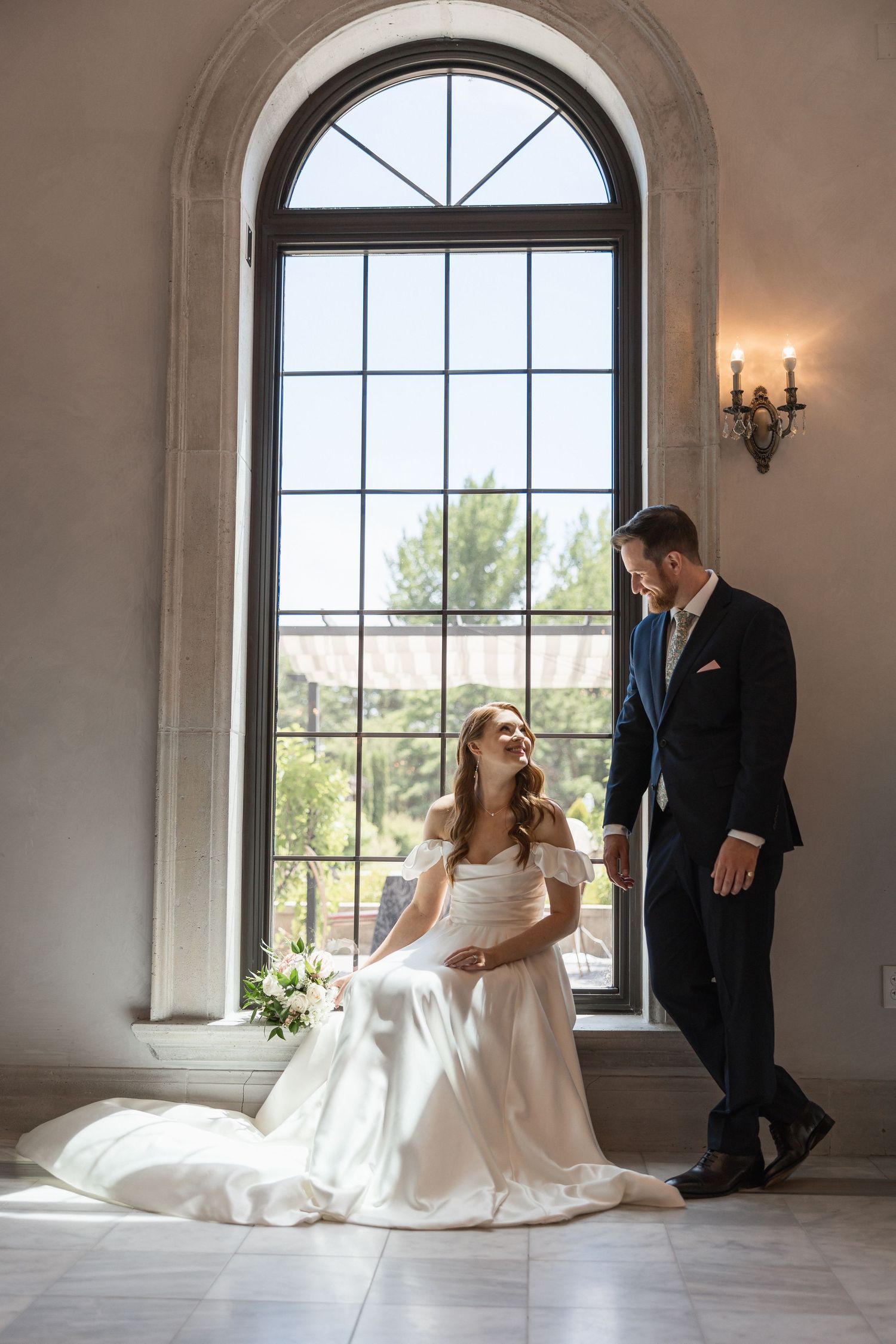 Romantic wedding photo sequence showing couple sitting by large arched windows in elegant room.